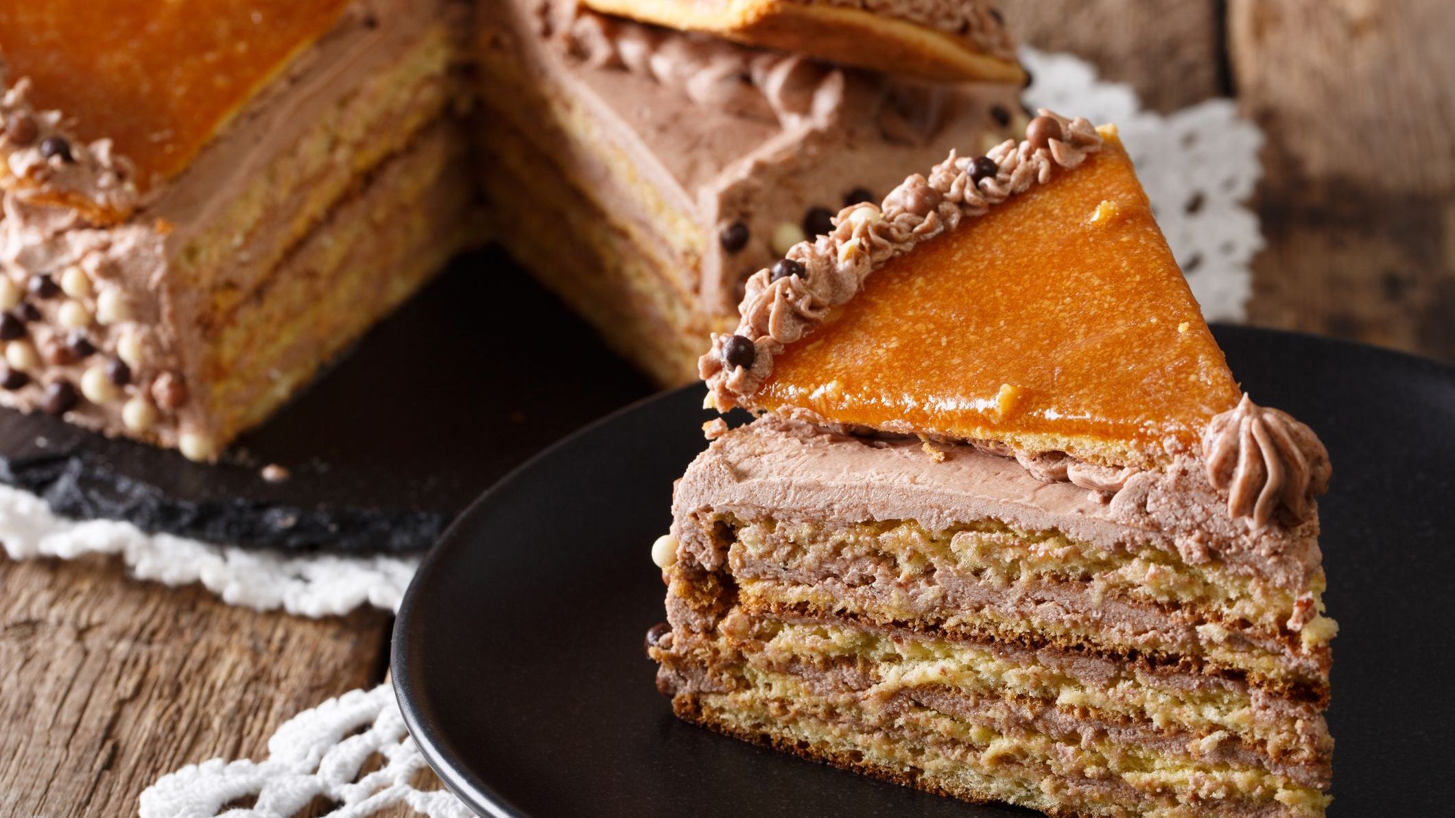 A close-up of a delicious slice of Hungarian Dobos cake with caramel on a black plate.