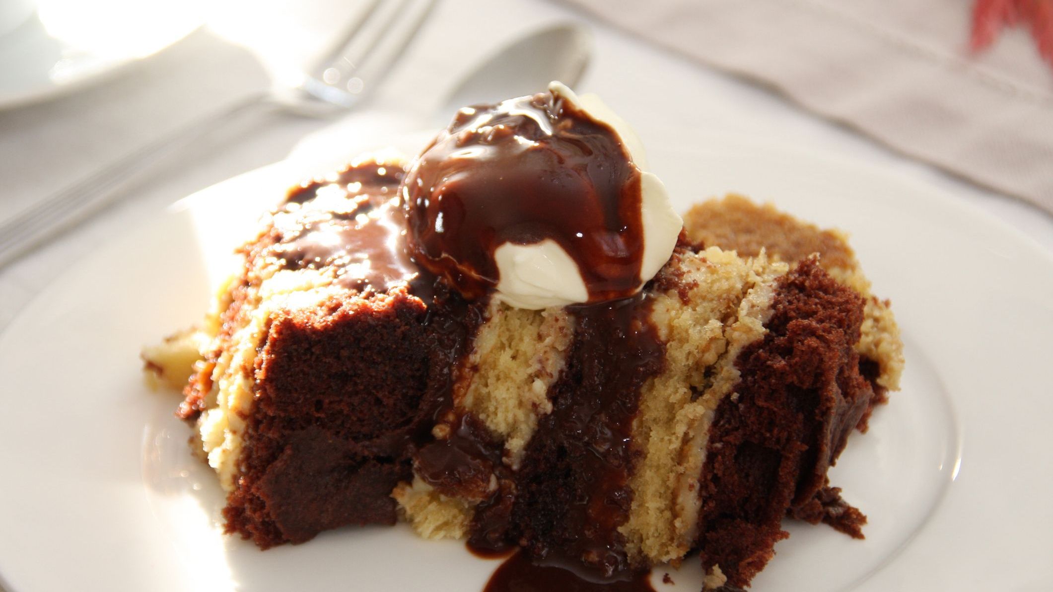 Layered cake served with chocolate sauce and whipped cream on a white plate.