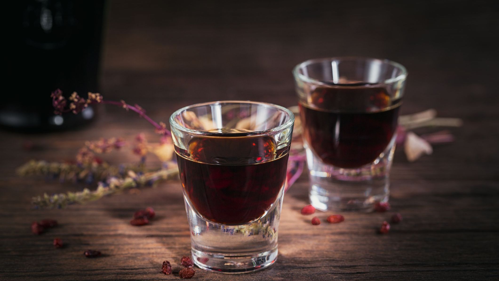 Two shots of a herbal bitter liqueur on a dark wooden background.