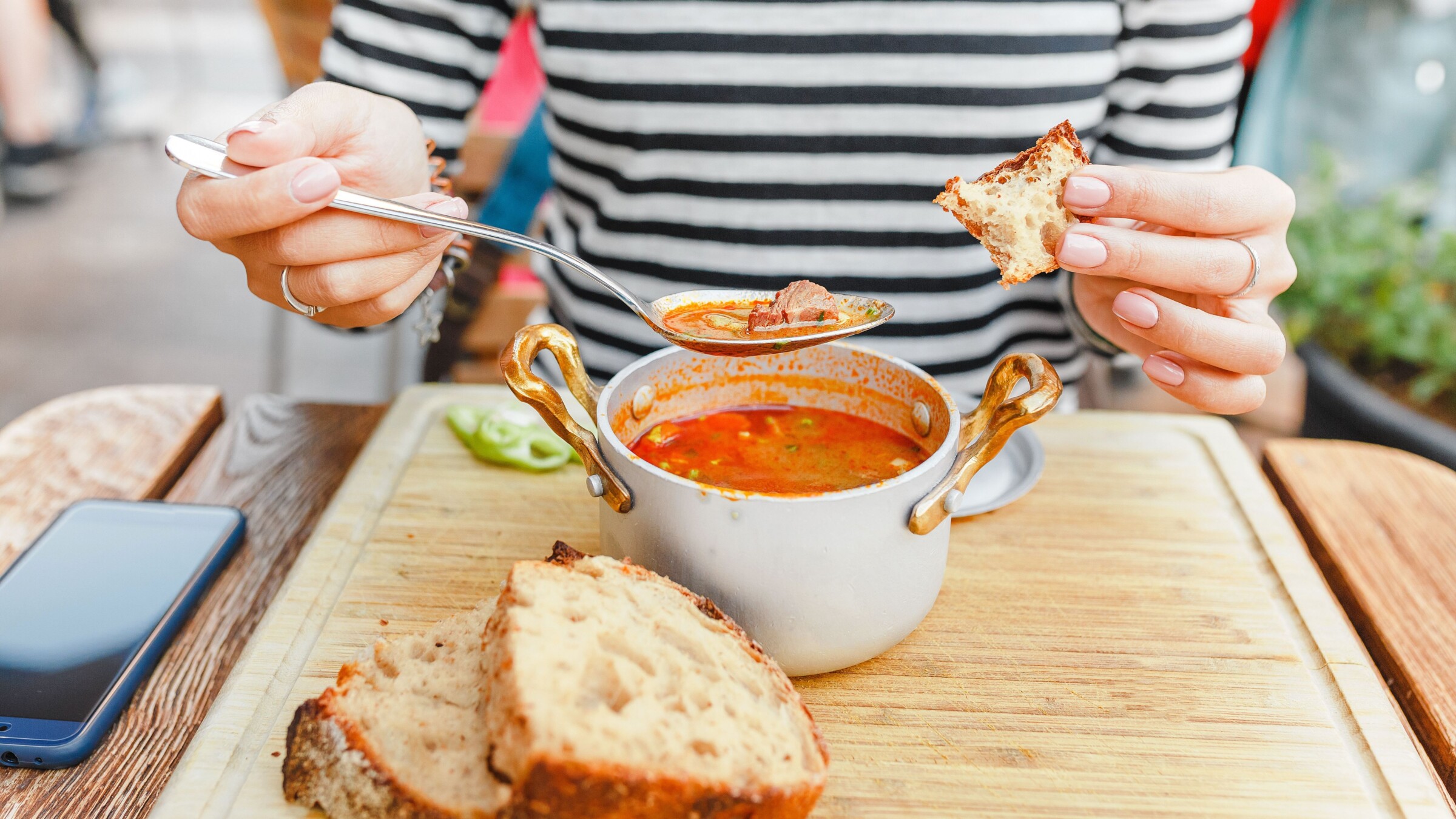 A woman eats a traditional Hungarian goulash or tomato soup from a saucepan in an outdoor restaurant.