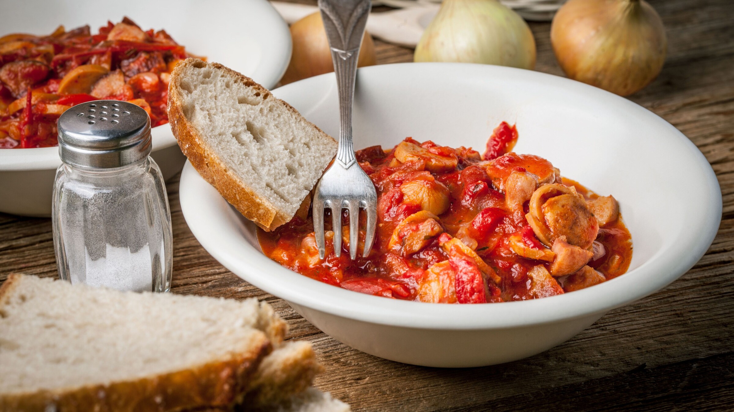 A white plate with a vegetable and sausage stew and a slice of bread on the side.