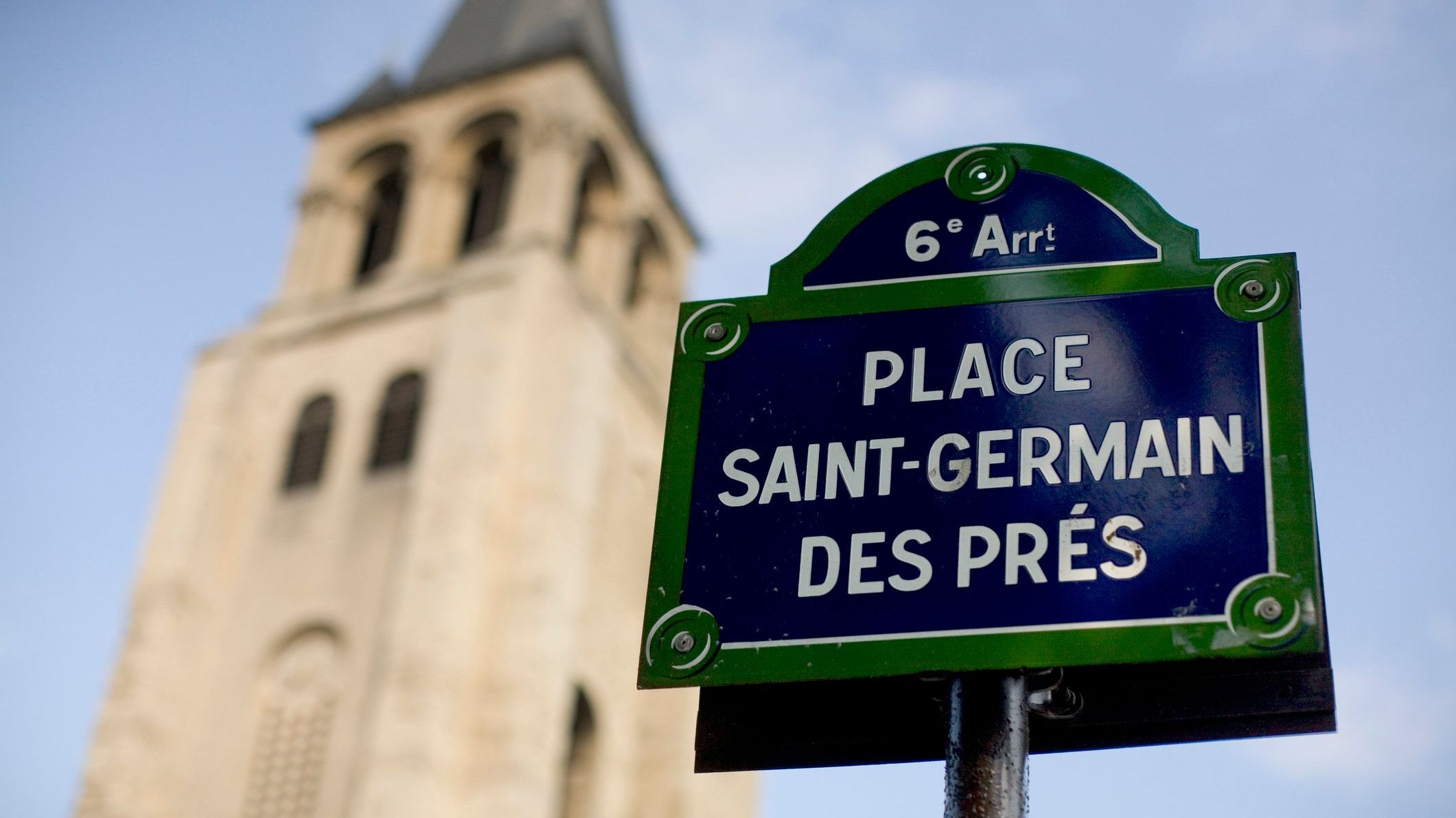 A street sign that reads Place Saint-Germain Des Pres with a bell tower in the background. 