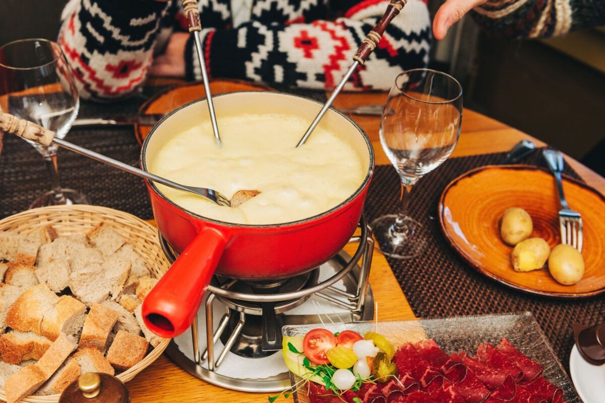 People sitting around a table with a red pot of cheese fondue.