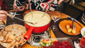 People sitting around a table with a red pot of cheese fondue.