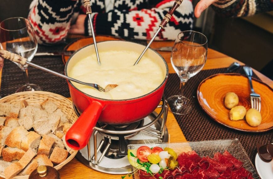 People sitting around a table with a red pot of cheese fondue.