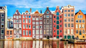 A row of typical Amsterdam buildings of various colors, lining a canal.