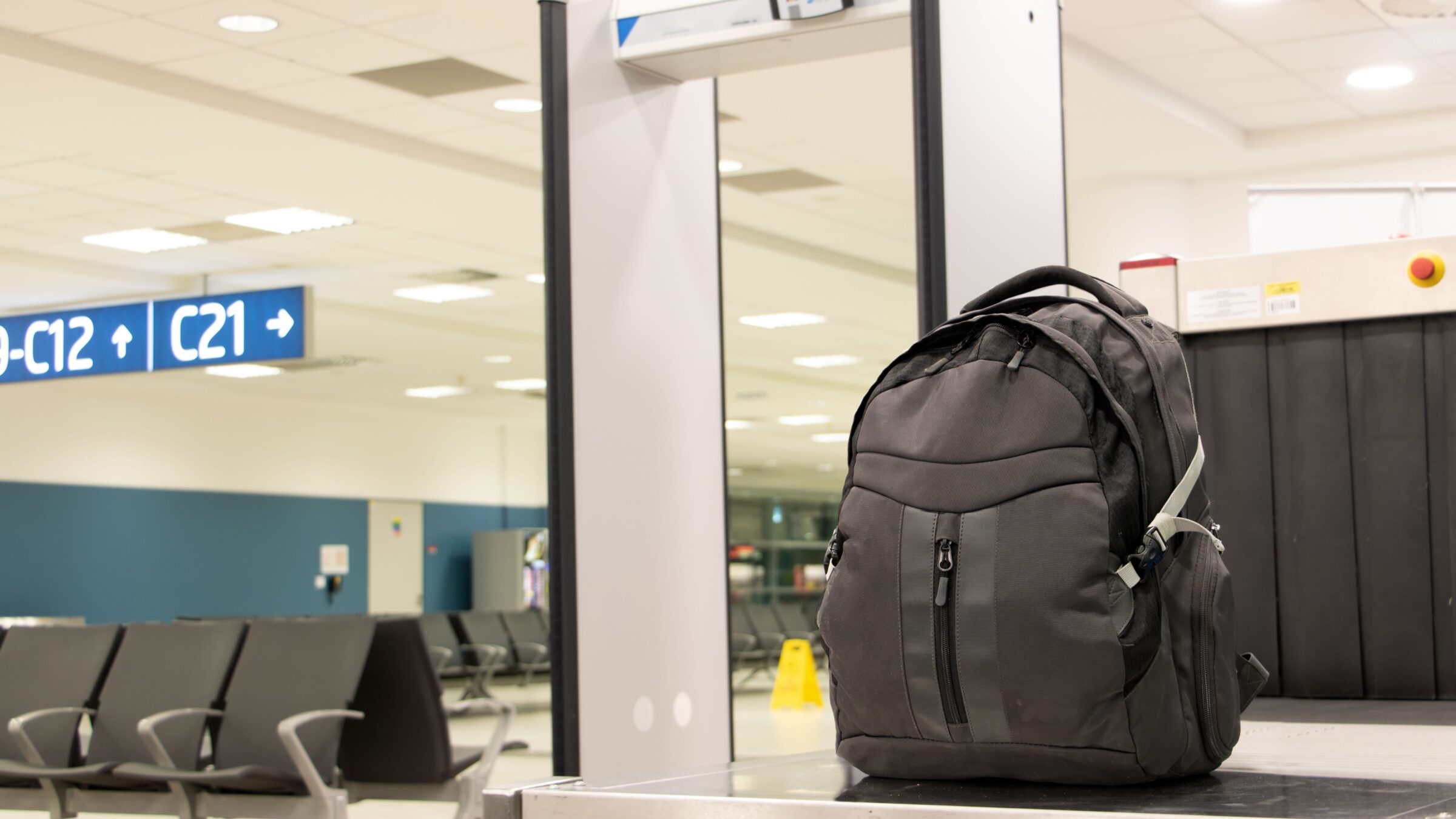 A backpack standing in front of a luggage scanner at the departure gate of an airport terminal.