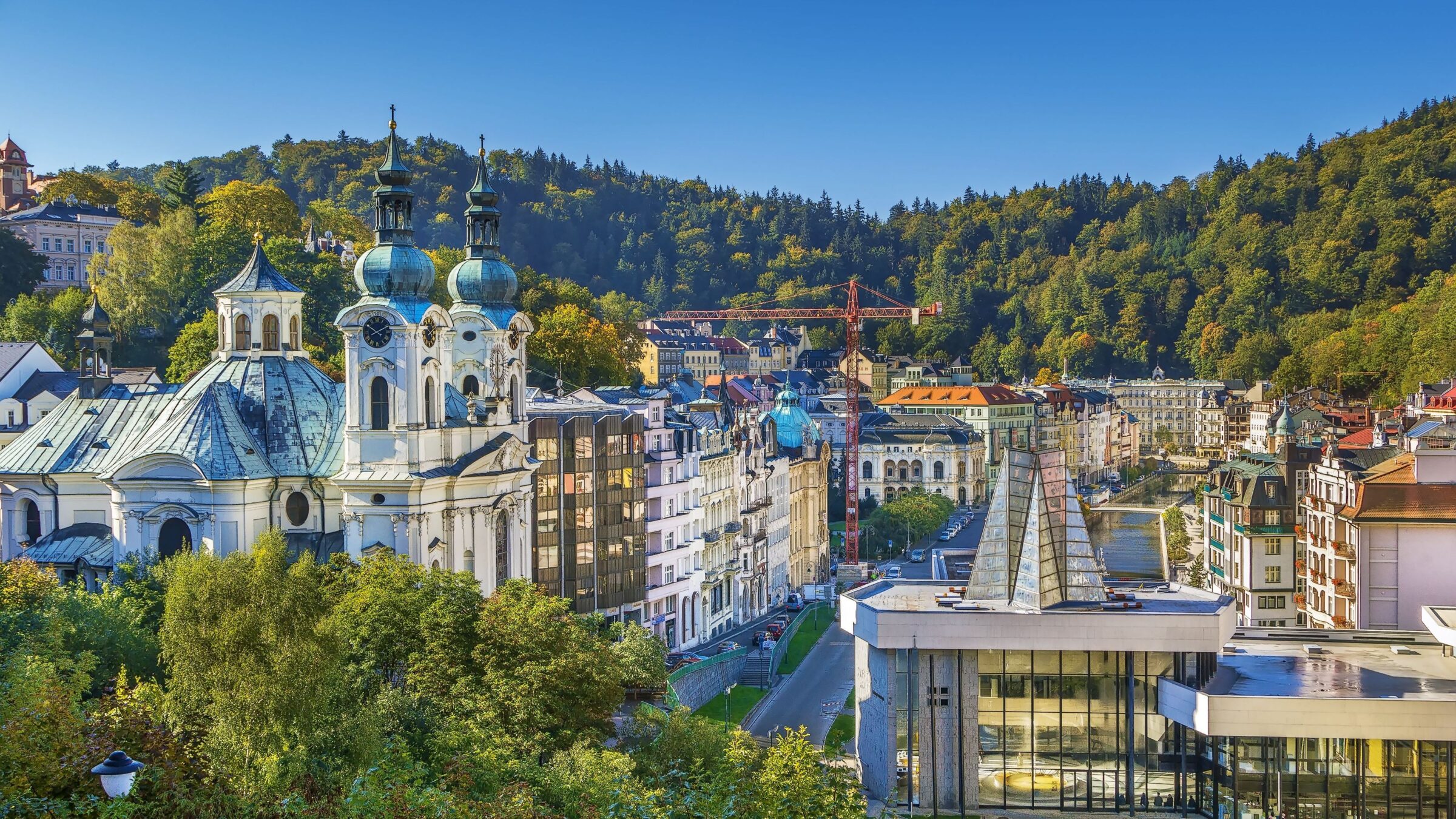 A panoramic view of Karlovy Vary with the church of Saint Mary Magdalene in the foreground and green hills in the distance.
