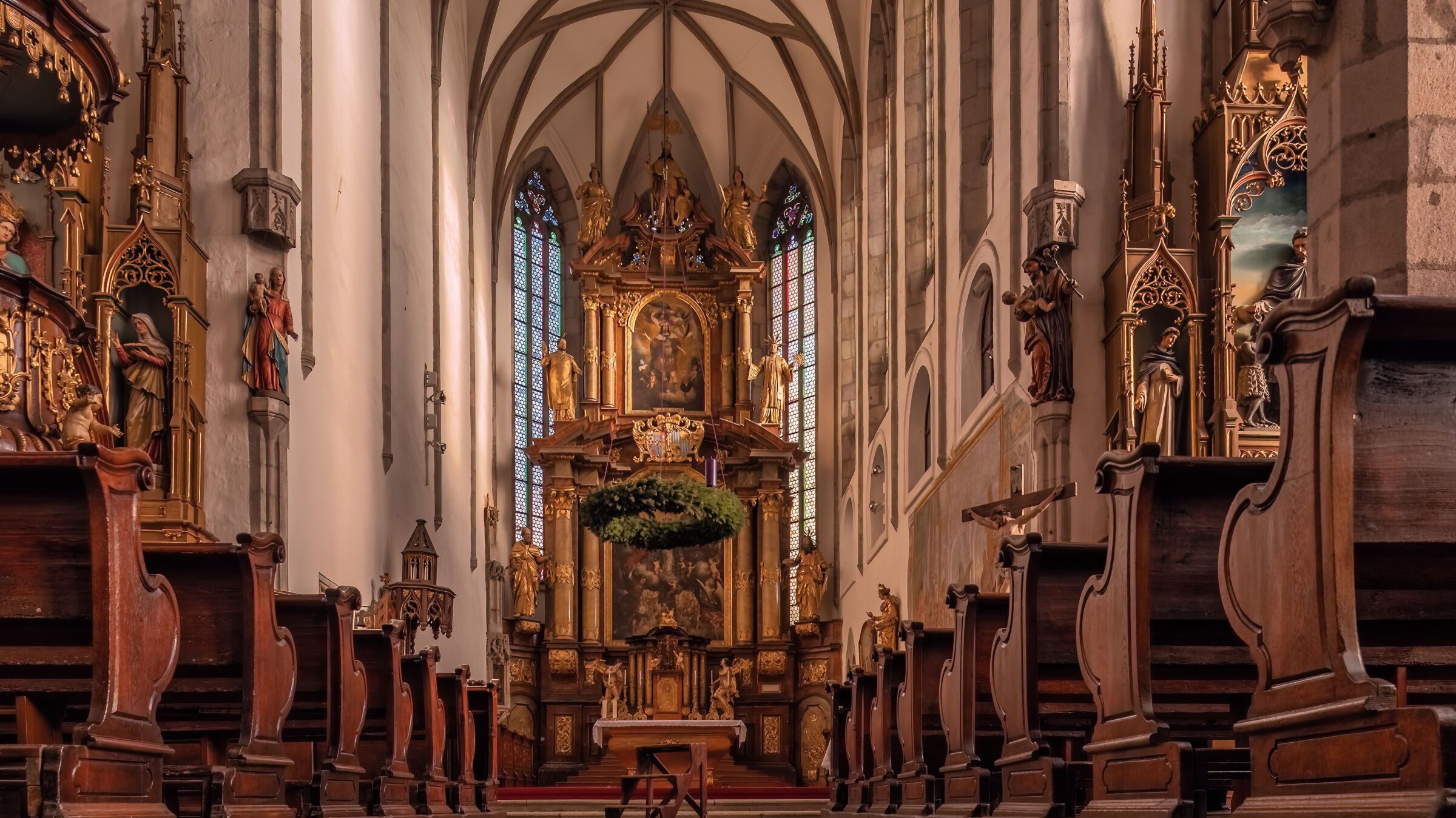 A stunning interior view of St. Vitus Church in Český Krumlov, showcasing its grand Baroque altar, intricate wooden pews, and elegant Gothic architecture. The warm lighting enhances the sacred and historic atmosphere of this religious landmark.