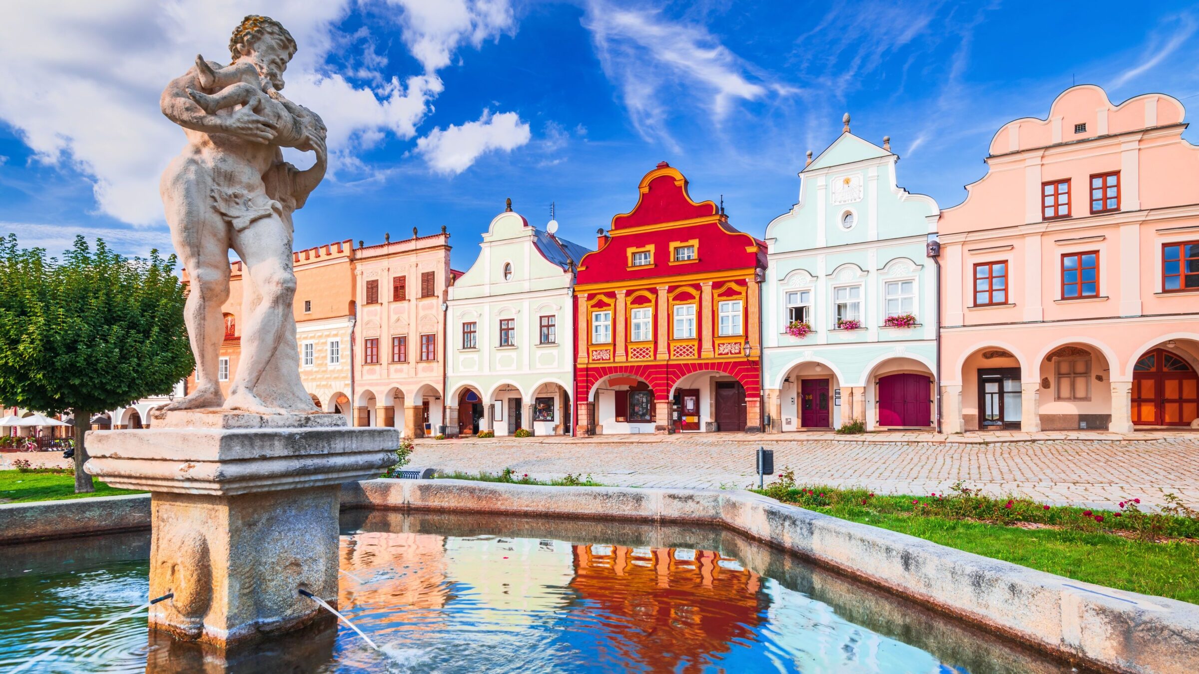 The main square of Telc with its famous 16th-century colorful houses, a UNESCO World Heritage Site, on a sunny day with blue sky and clouds.