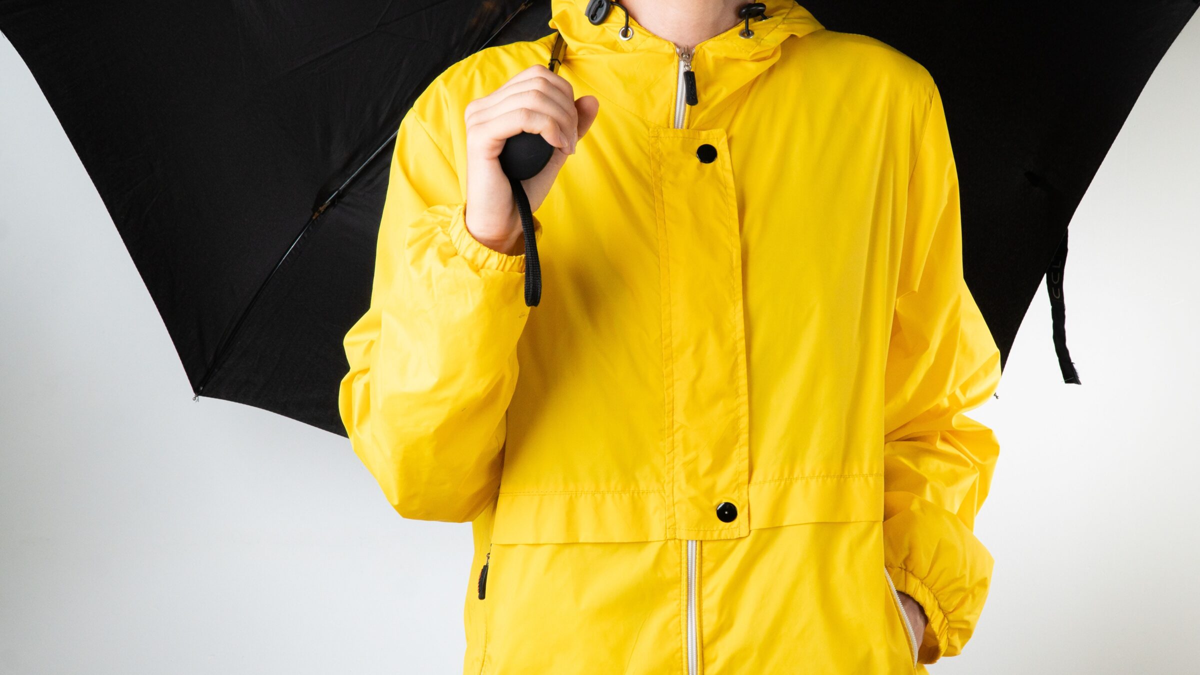A woman in yellow raincoat holds a black umbrella on a white background.