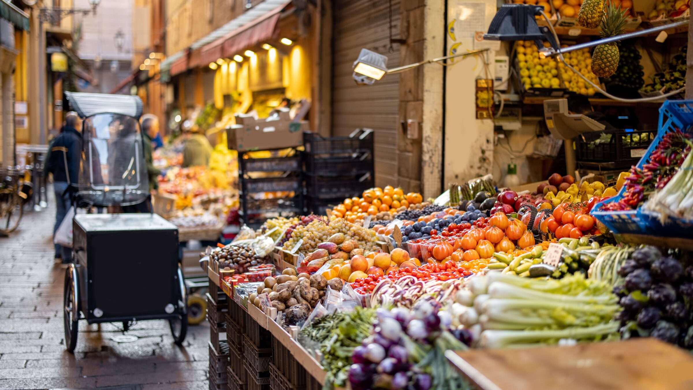 Stalls with fresh fruit and vegetables along a cobbled street. 