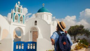 A woman with her back turned to the camera is admiring a whitewashed church in Santorini.