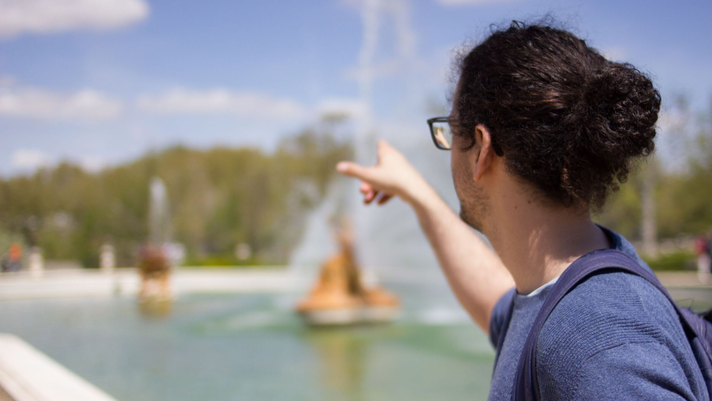 A young man pointing at a fountain with his back turned to the camera. 
