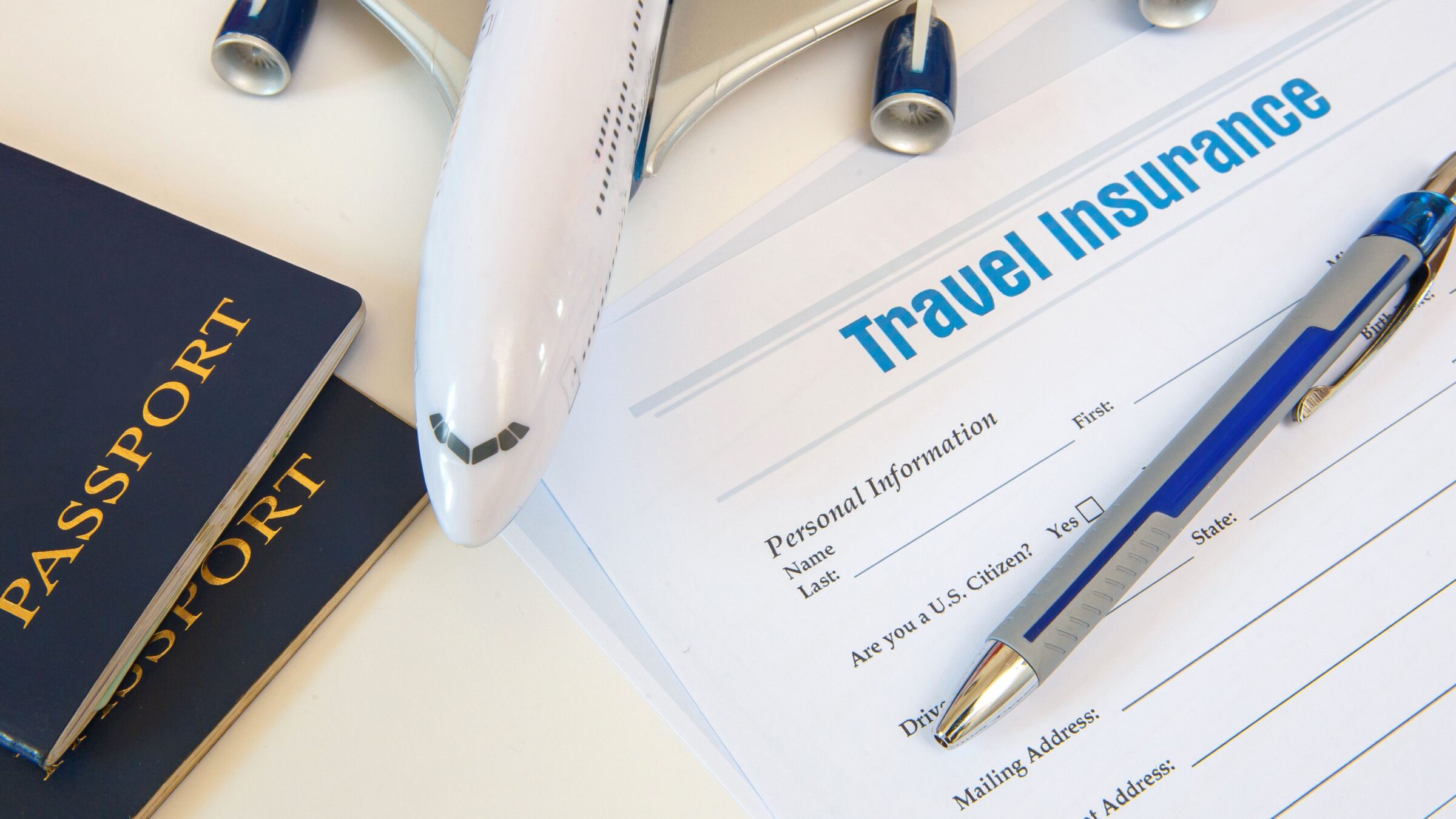 A travel insurance application form, two passports, a pen and a toy airplane.