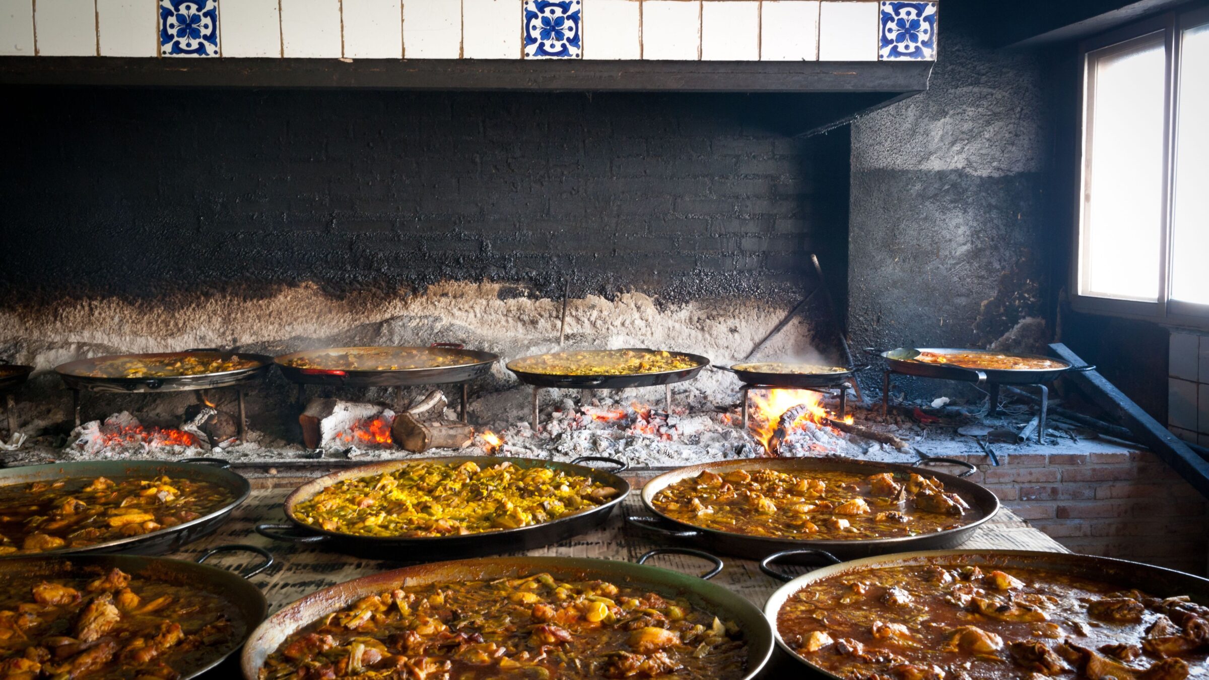 Several trays of paella cooked on fire. 