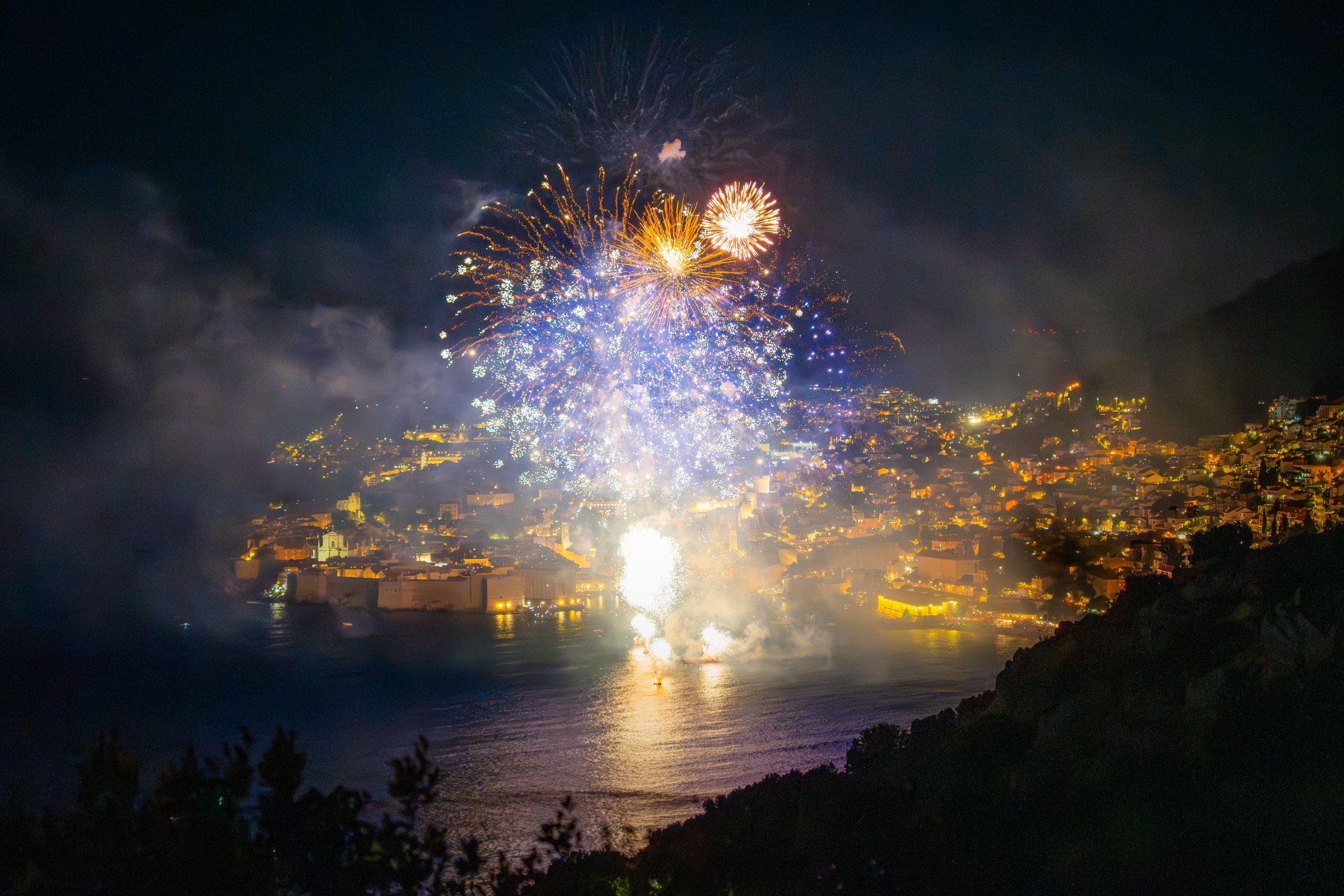 A panoramic night view of Dubrovnik with many fireworks illuminating the sky. 
