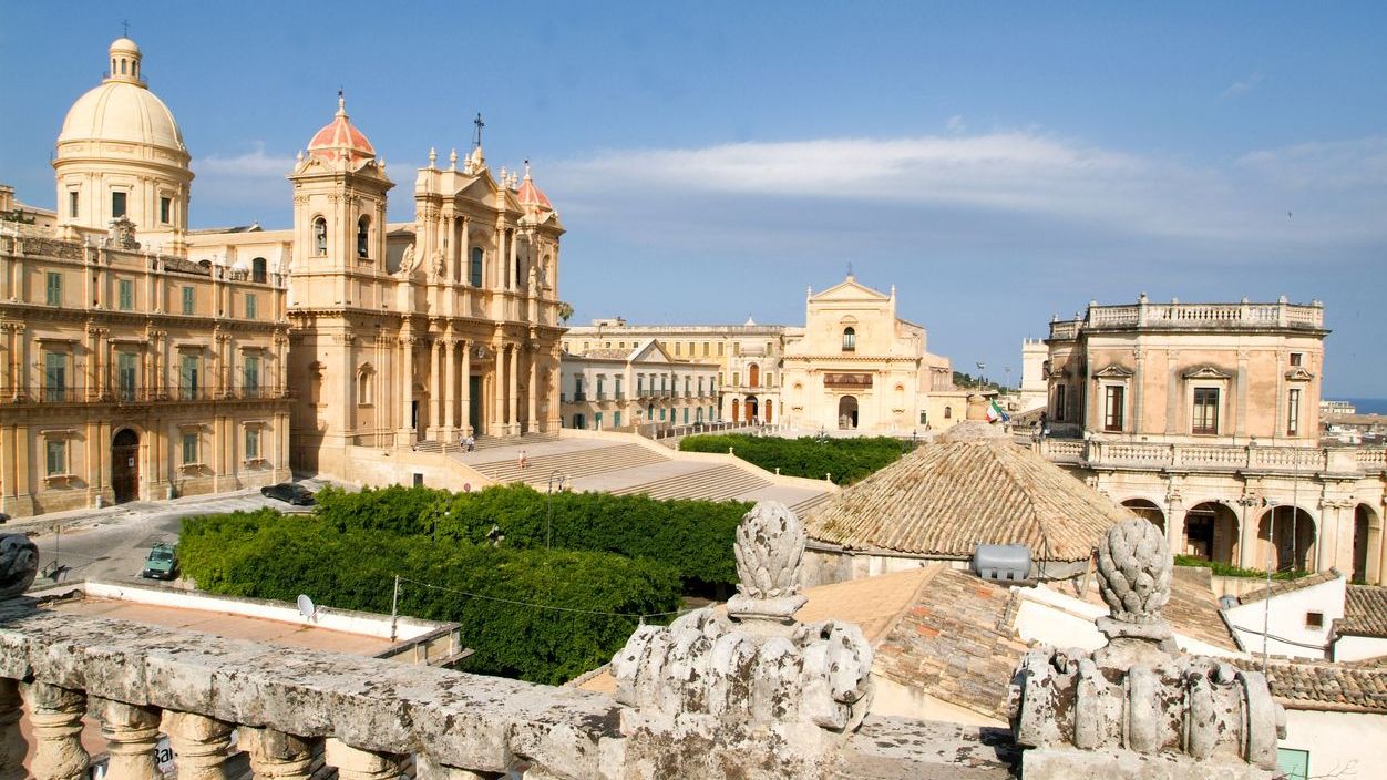 Various Baroque buildings under a bright blue sky in Noto, one of the must-visit places in Sicily. 