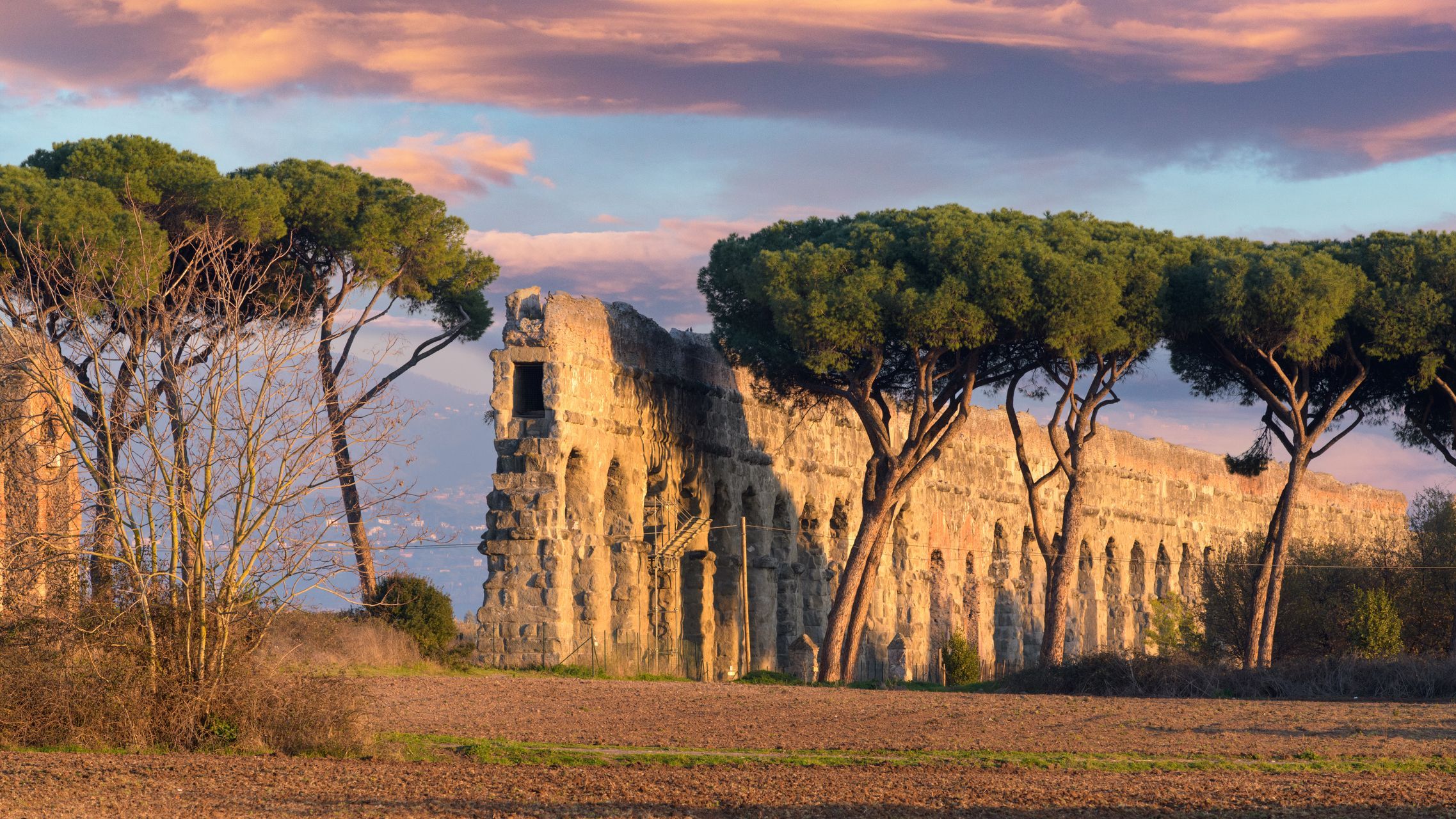 The remains of a Roman aqueduct among trees under a dramatic sky. 