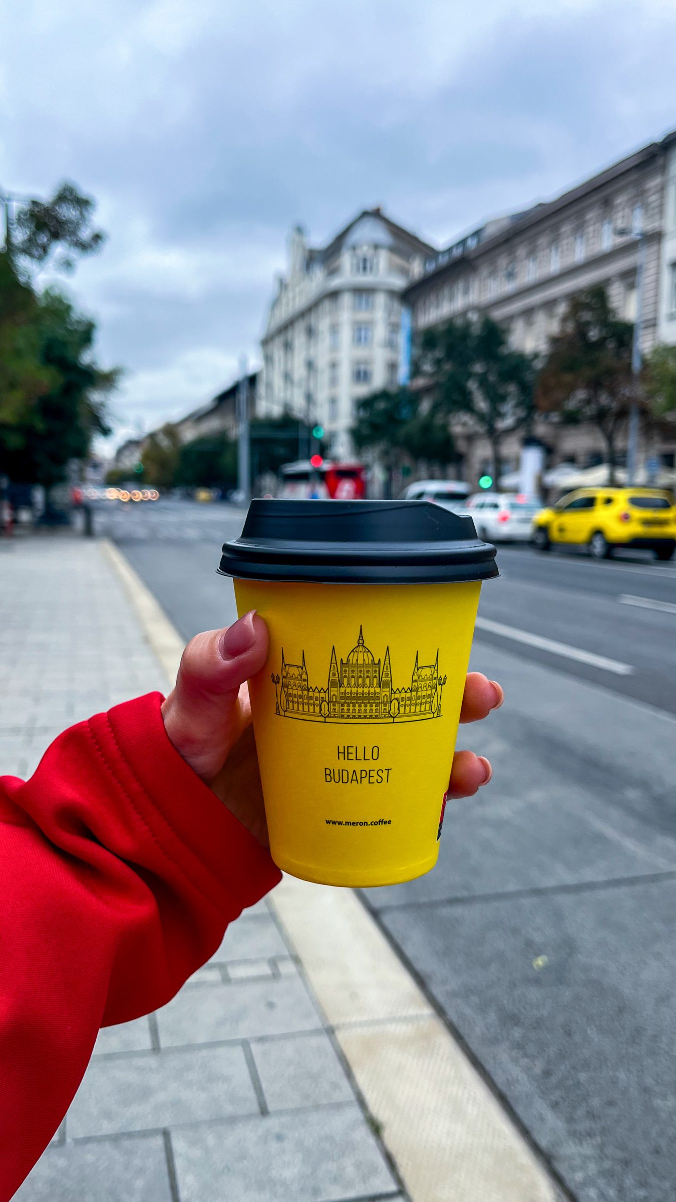 A close-up of a woman's hand holding a yellow paper coffee cup. 