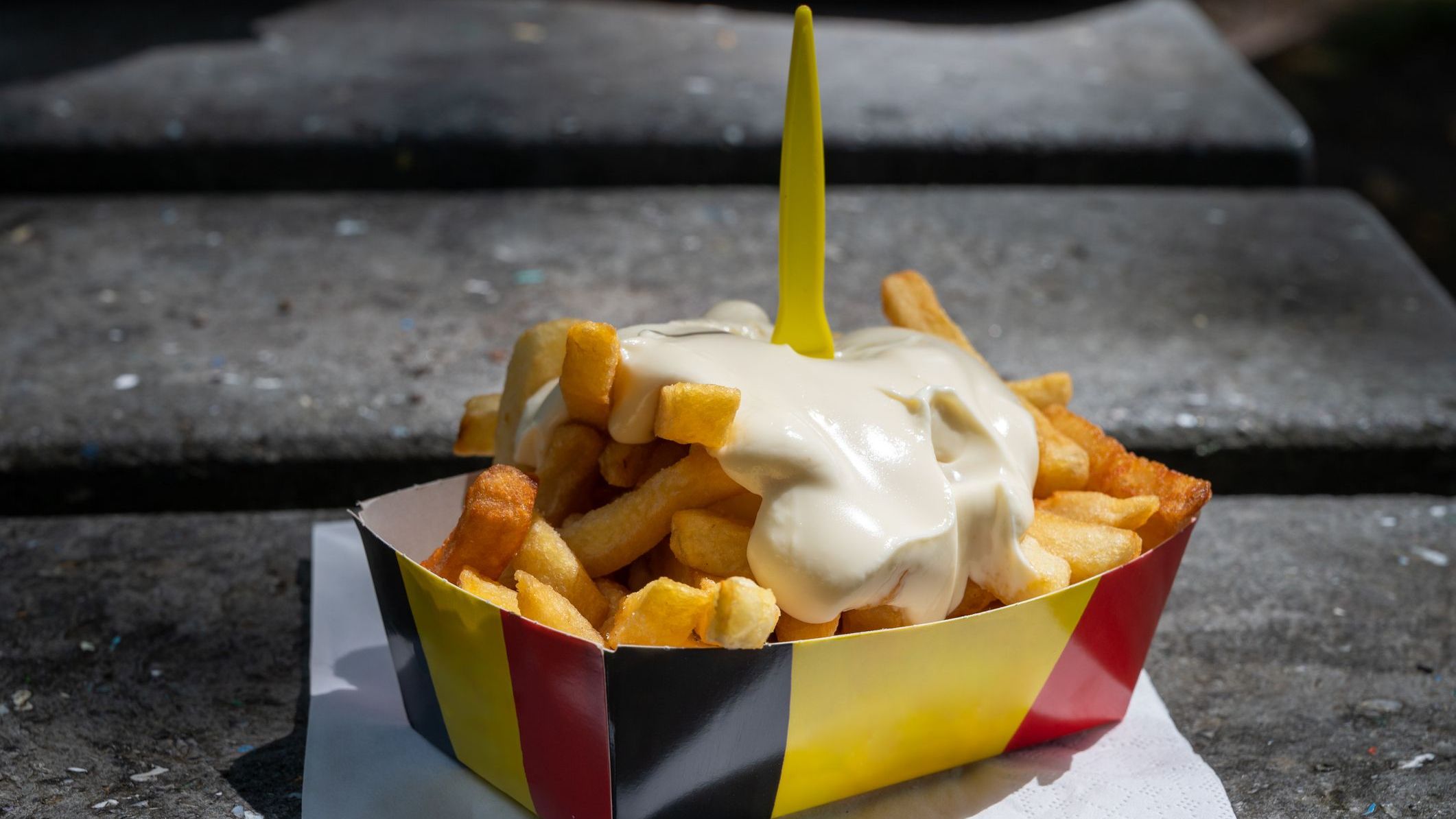 A paper box in the colors of the Belgian flag filled with fries topped with mayonnaise, probably the best Belgian food.