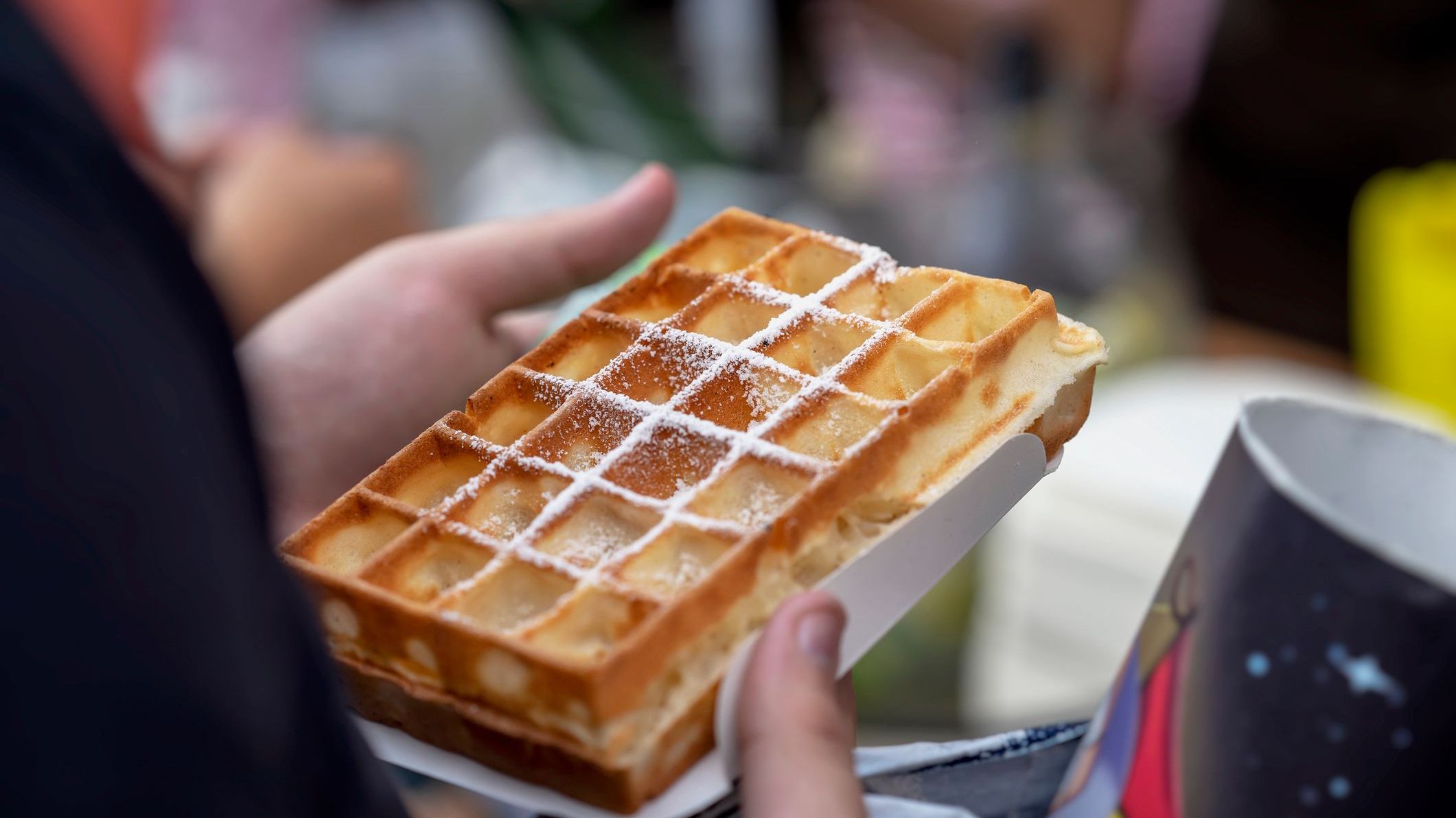 A warm, freshly baked Belgian waffle with powdered sugar in the hands of the buyer.