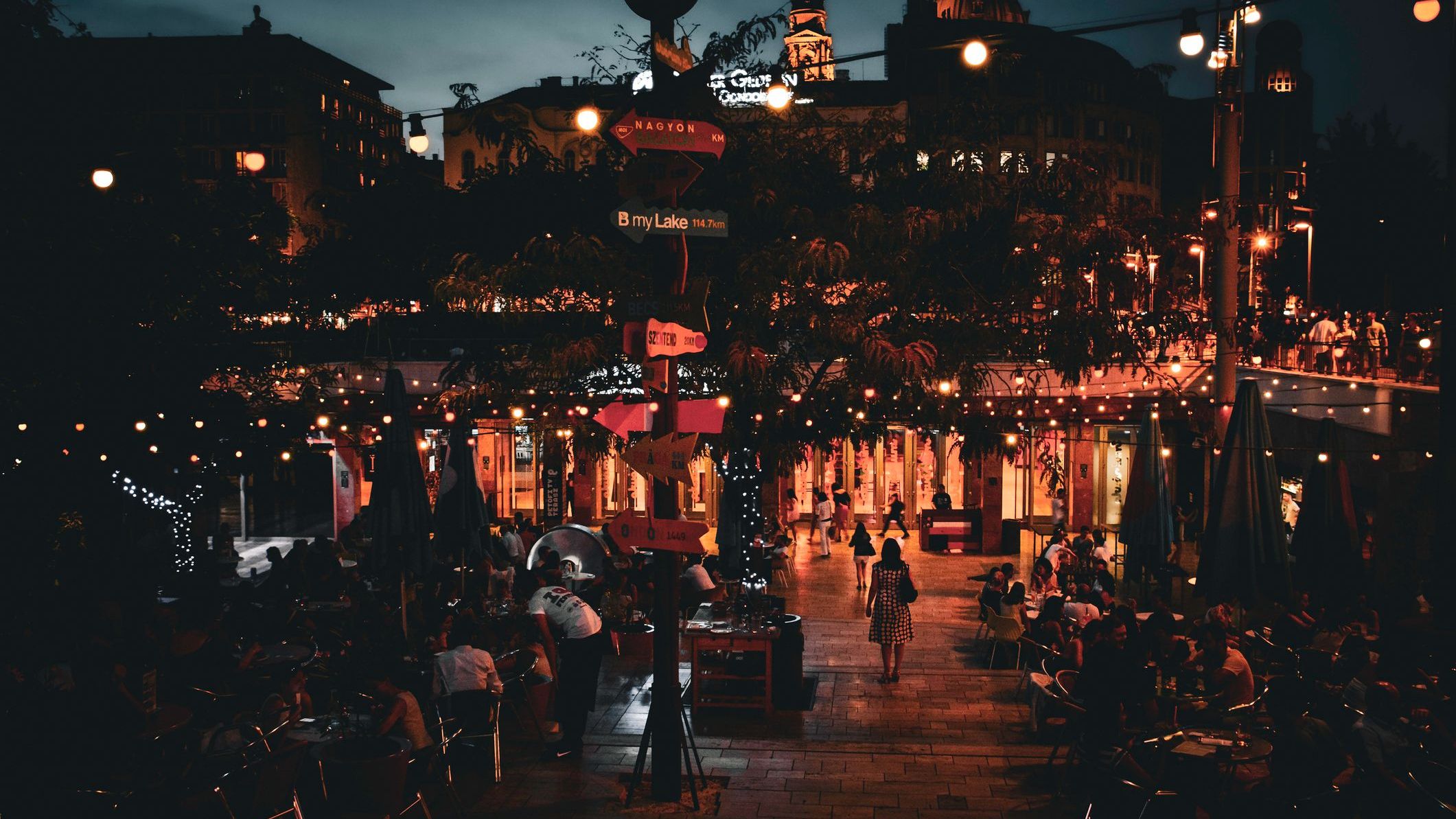 A night shot of Budapest with people eating and drinking at outdoor establishments. 