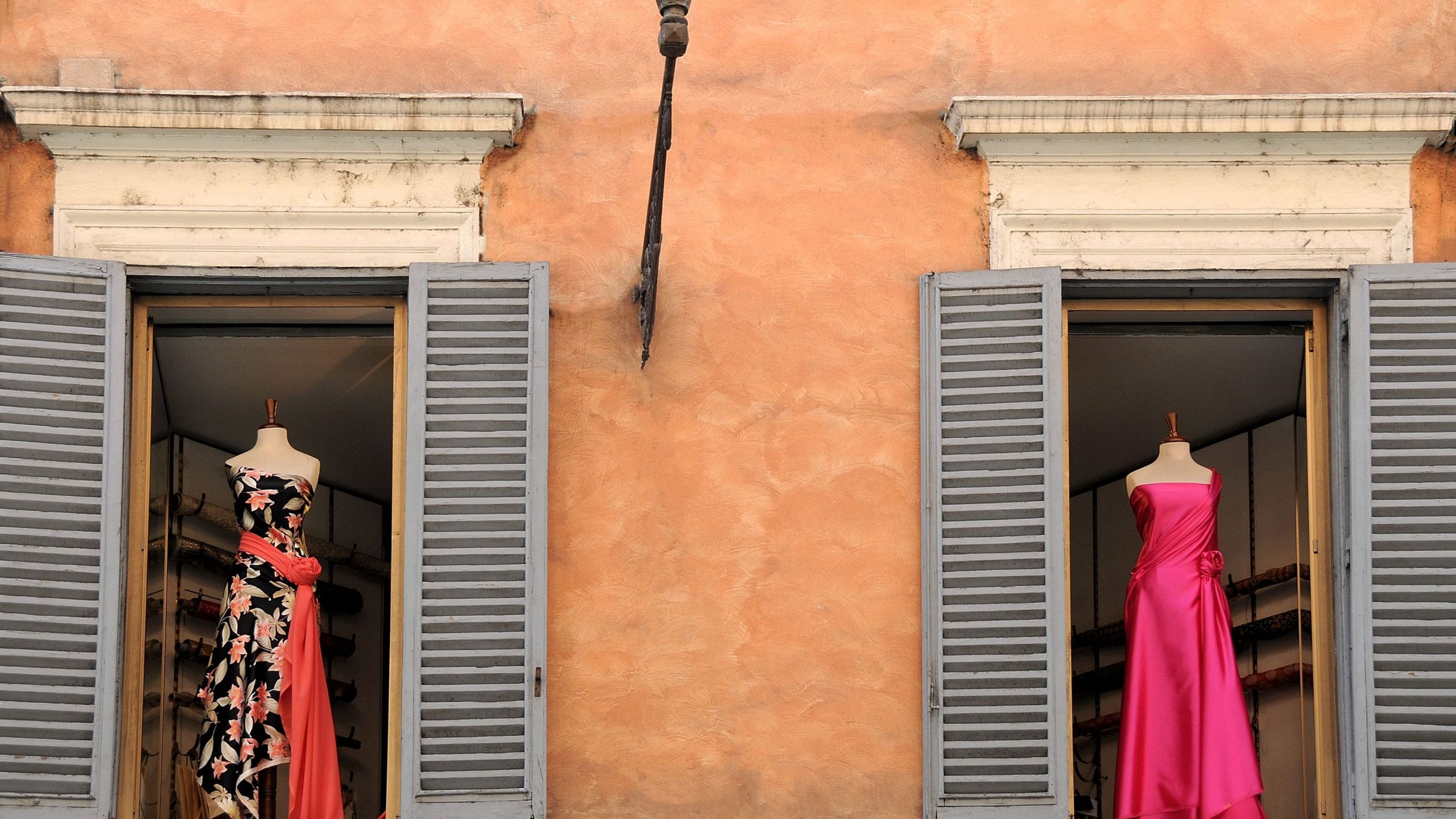 Two dresses displayed on two windows of an old Italian building. 
