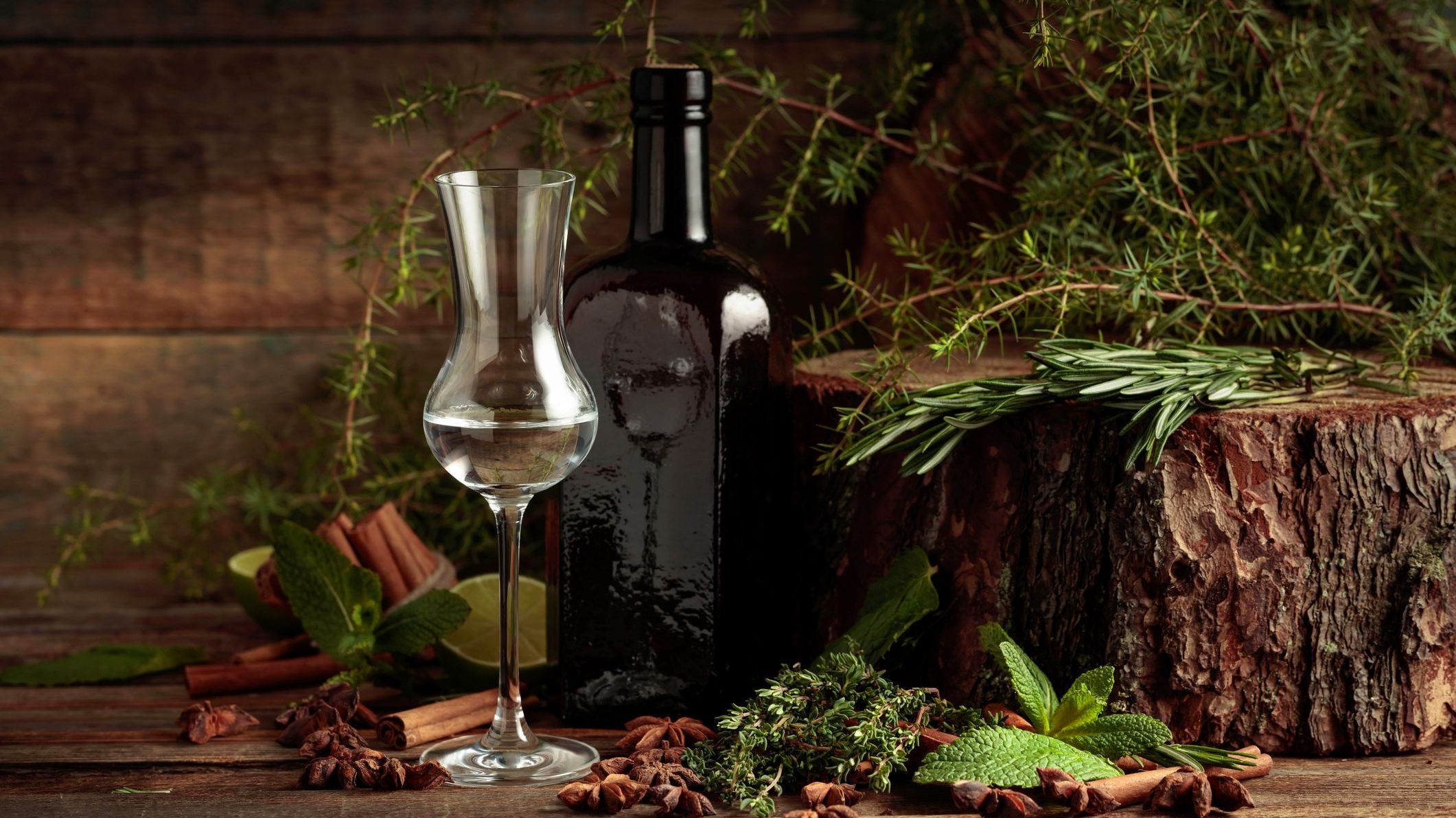 A vintage bottle and a tulip-shaped glass of gin on an old wooden table.
