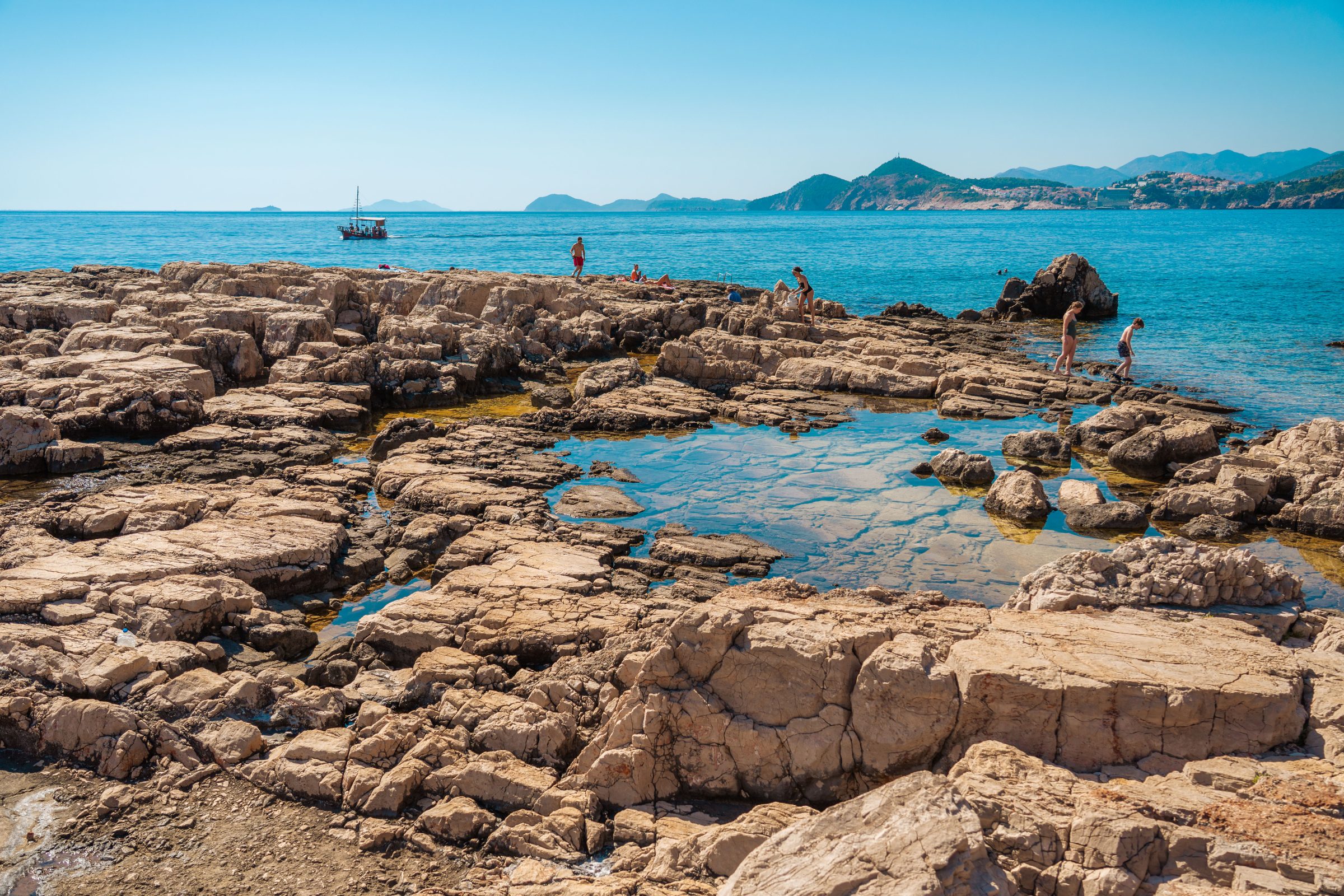 Rocks and the sea. Some people are walking on the rocks and there's a small boat in the distance.