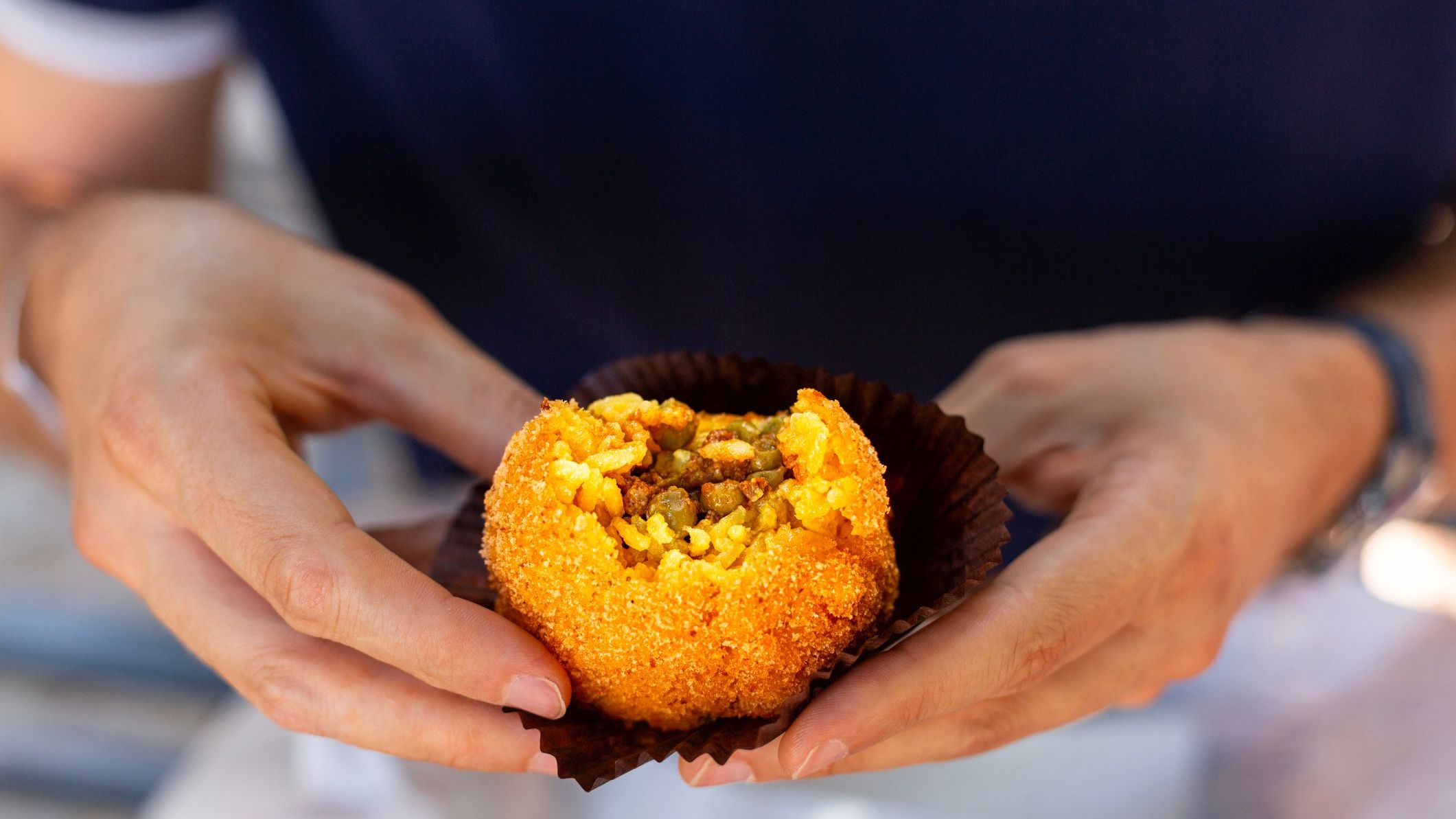 A man is eating arancini, an Italian rice ball al ragu or al sugo, that is stuffed  with meat, peas, tomato sauce and spices, coated with breadcrumbs and deep fried. 