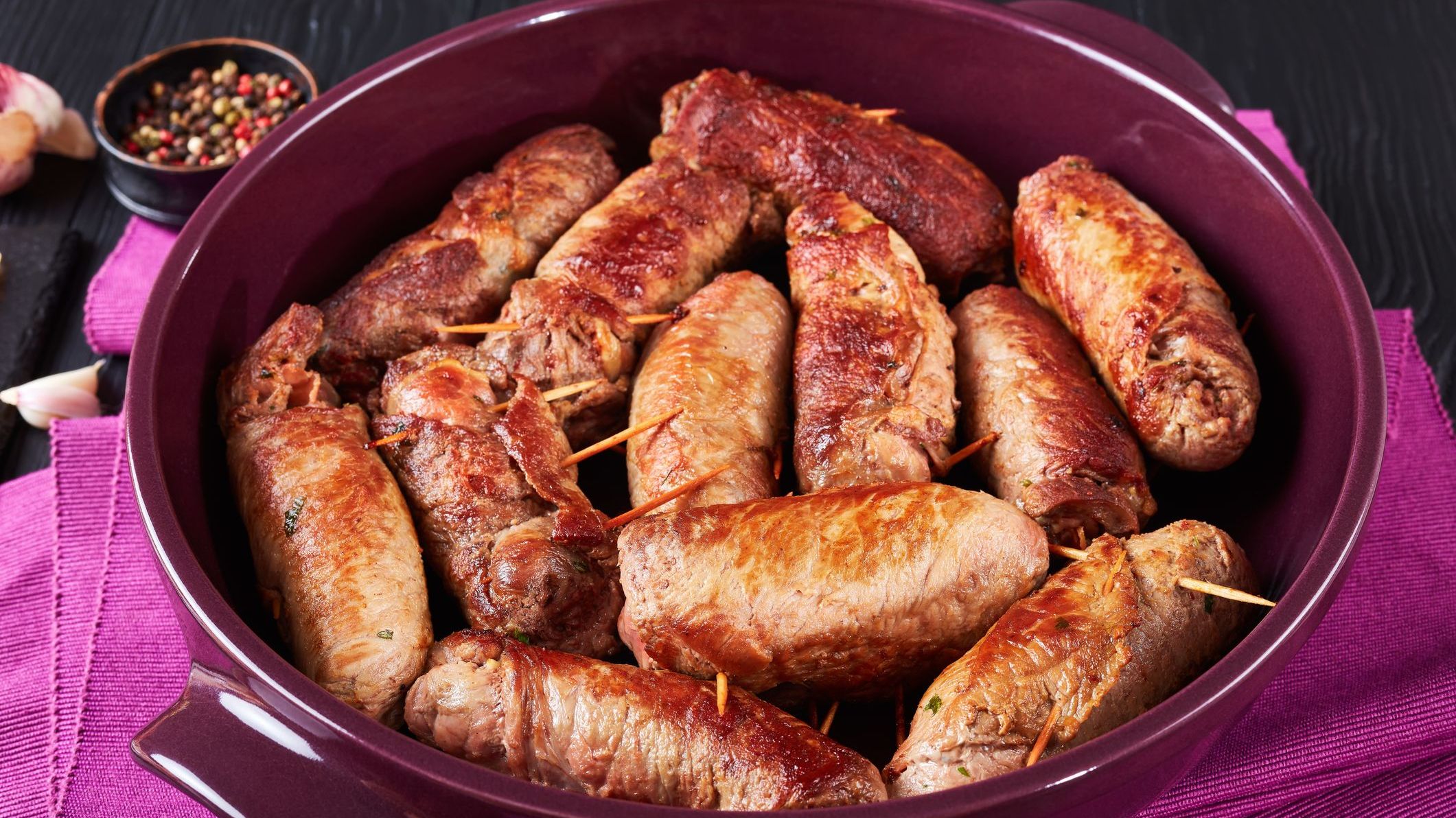 A close-up of fried Italian Braciole: beef steak rolls stuffed with sliced prosciutto, grated parmesan cheese and parsley, pinned with toothpicks.