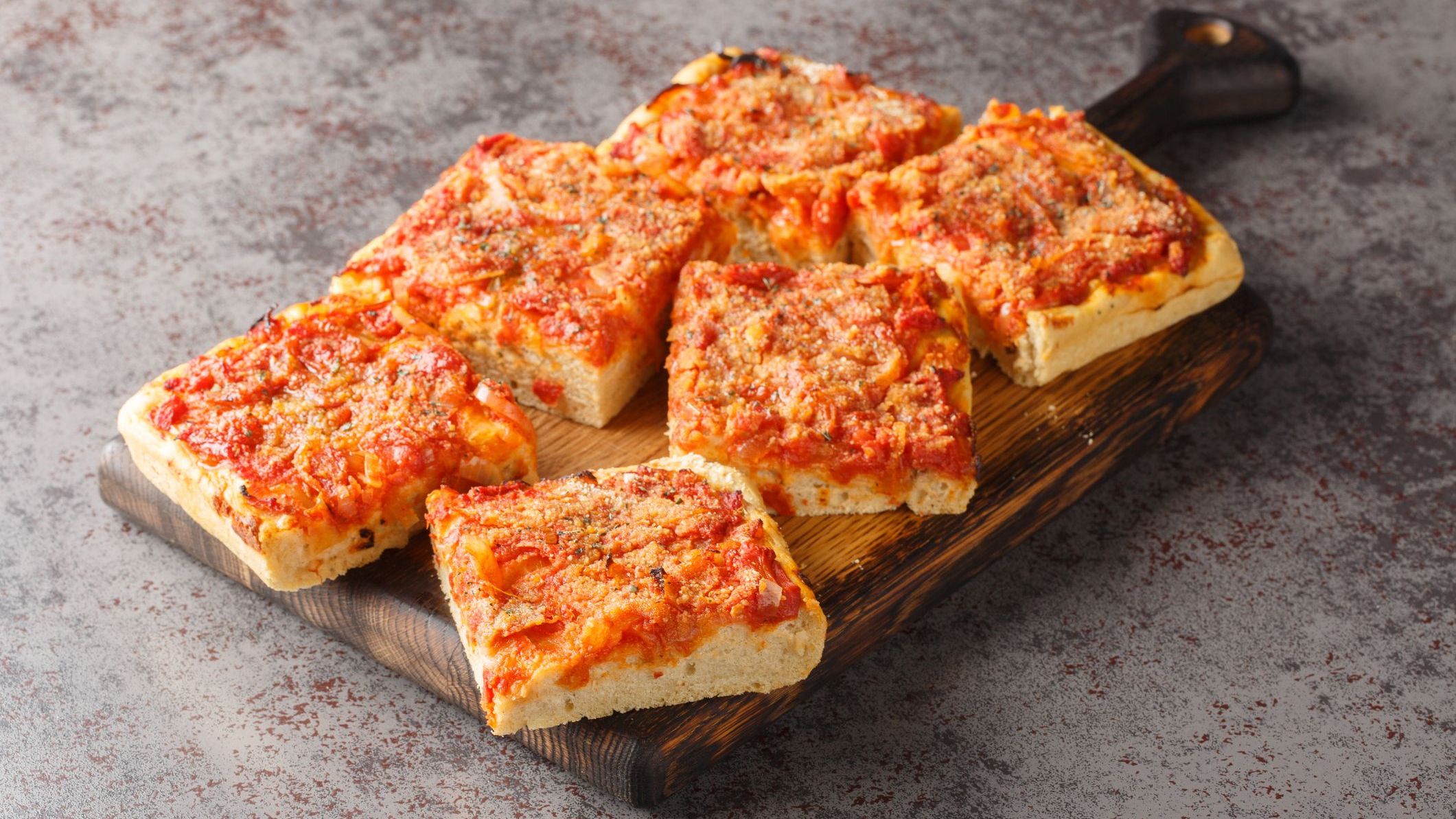 A close-up of Sfincione, a typical oven-baked focaccia, which is very soft and seasoned with tomato, onion, anchovies, cheese, oregano and bread crumbs, among the best food in Sicily. 