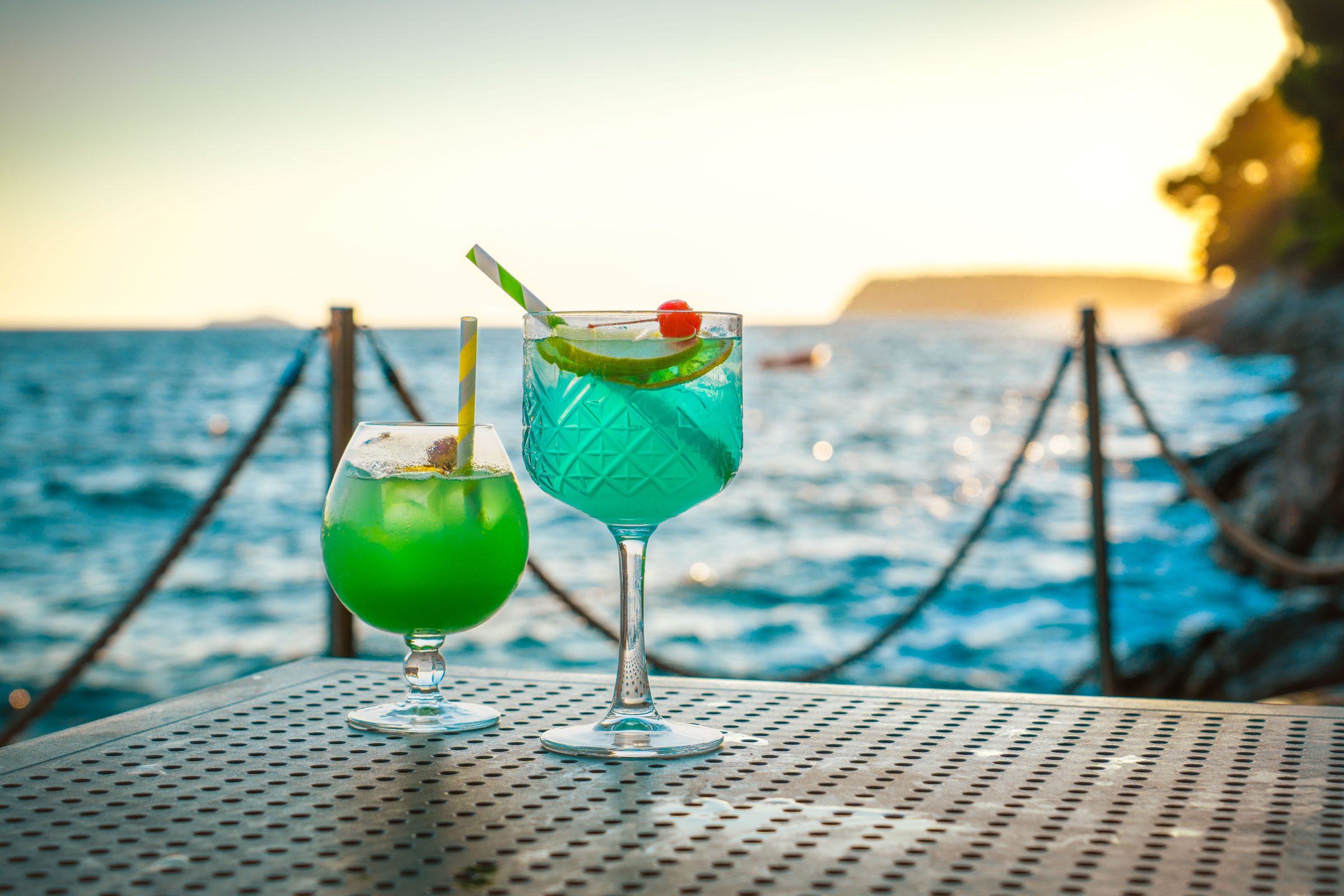 Two cocktails on a table with the sea in the background. 