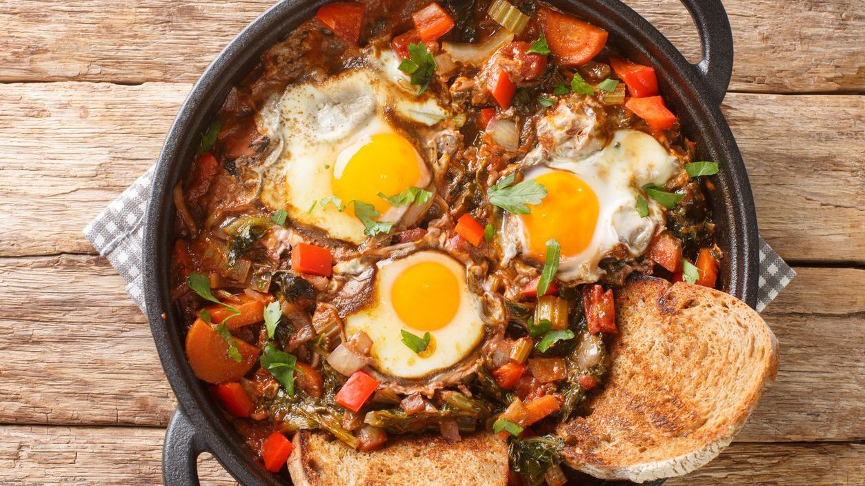 A clay pot with a soup topped with three eggs and two slices of toasted bread.