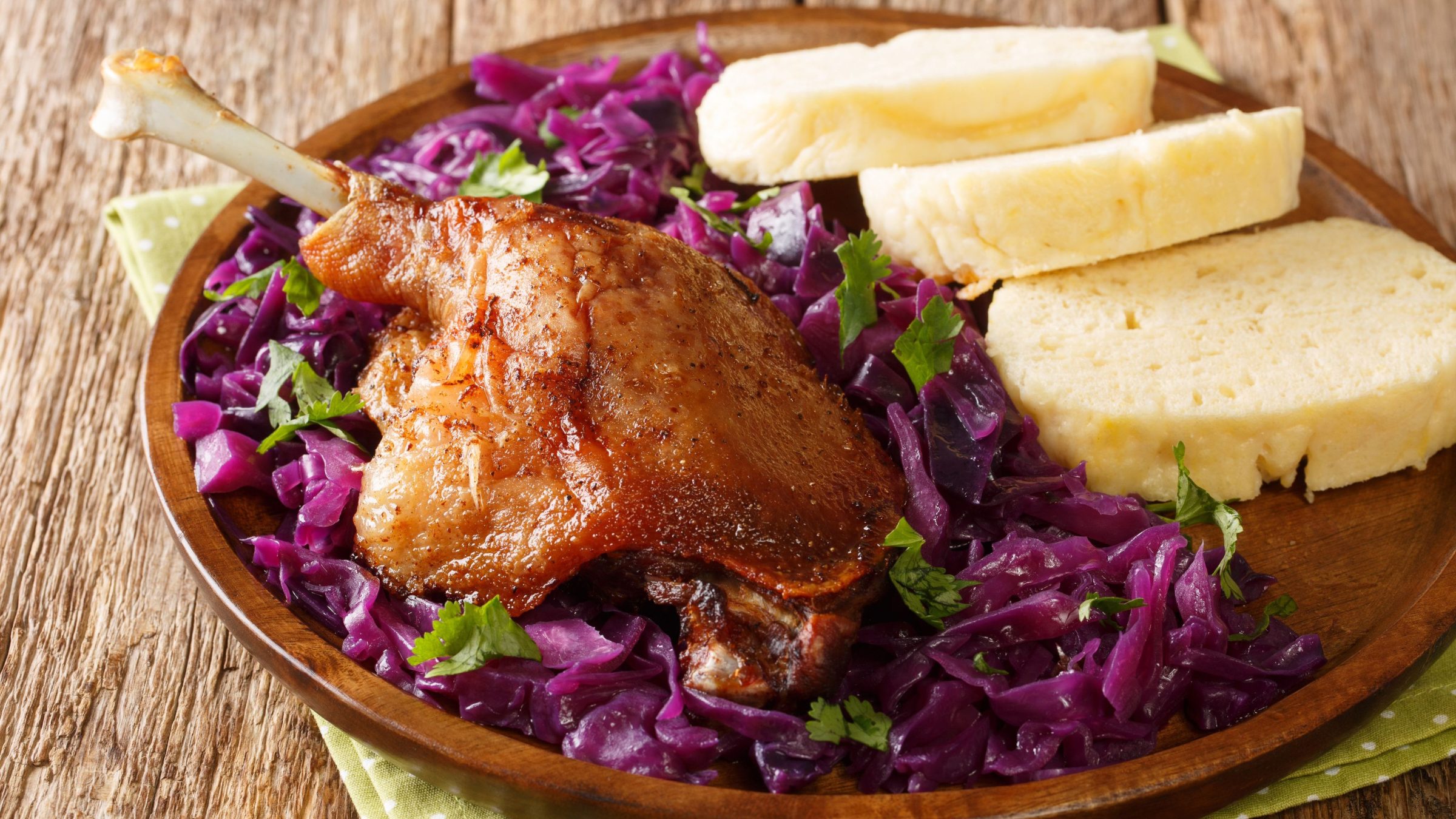 A brown plate with a roast duck leg, cabbage, and bread dumplings. 