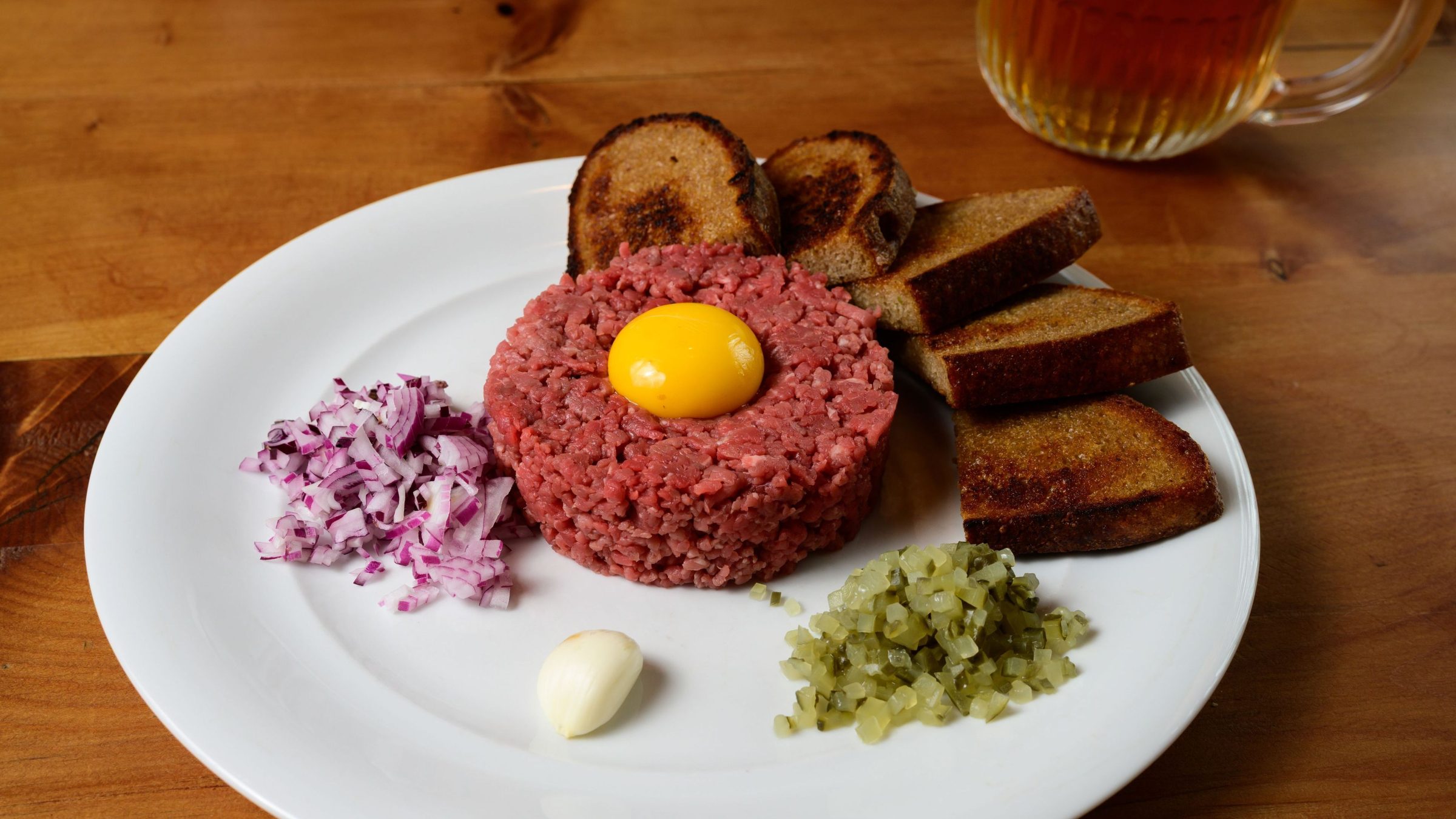 A white plate with beef tartare topped with an egg and served with slices of toasted bread. 