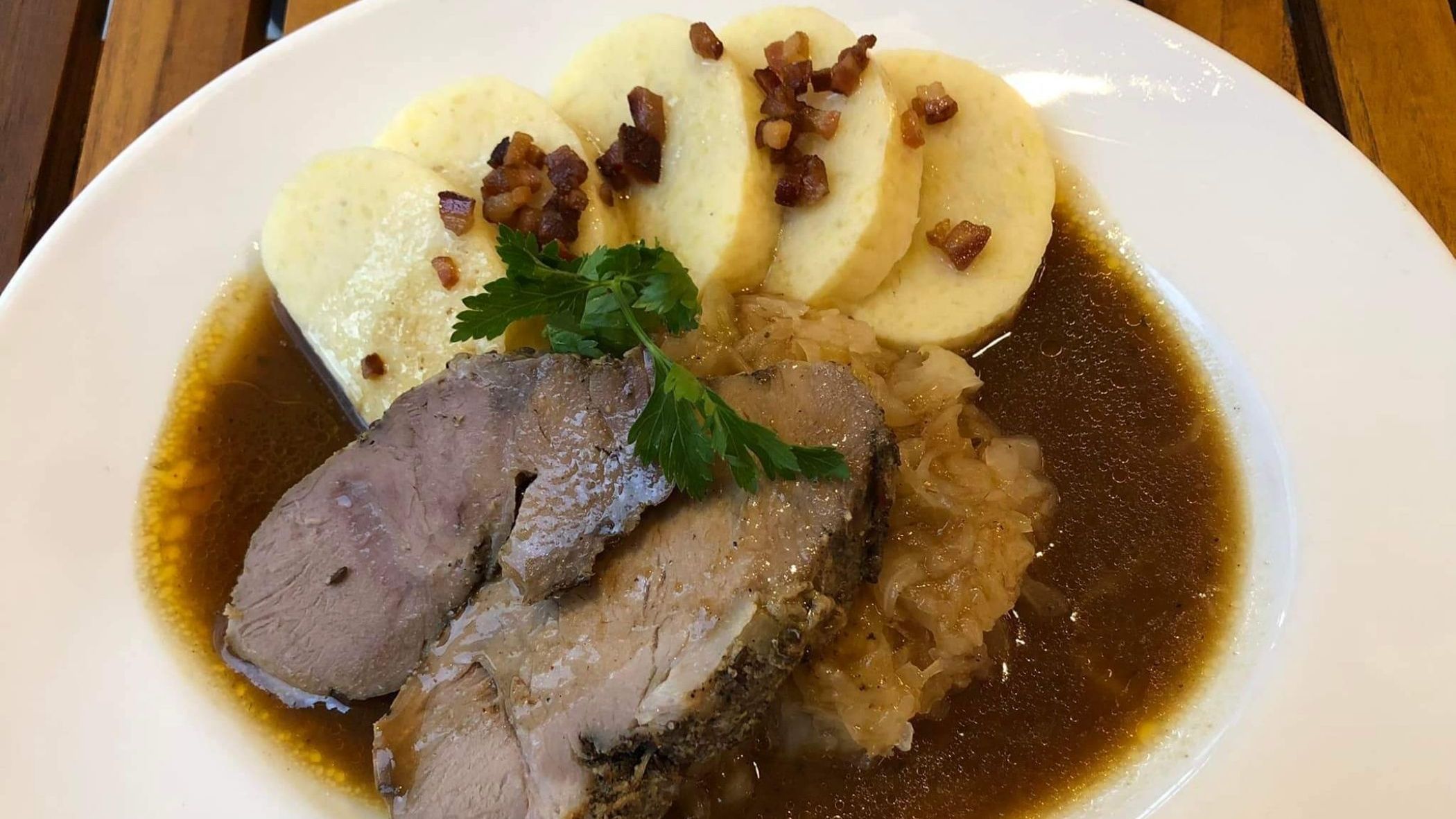 A close-up of a white plate with pieces of meat and bread dumplings in a brown sauce. 