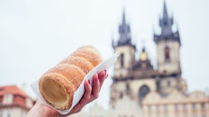 A woman's hand is holding a chimney cake with the Church of Our Lady Before Tyn in the background.