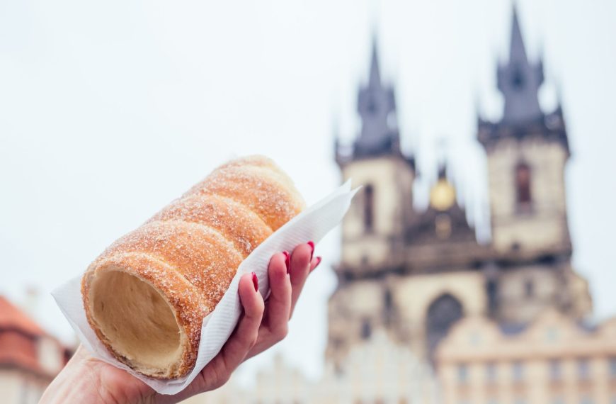 A woman's hand is holding a chimney cake with the Church of Our Lady Before Tyn in the background.
