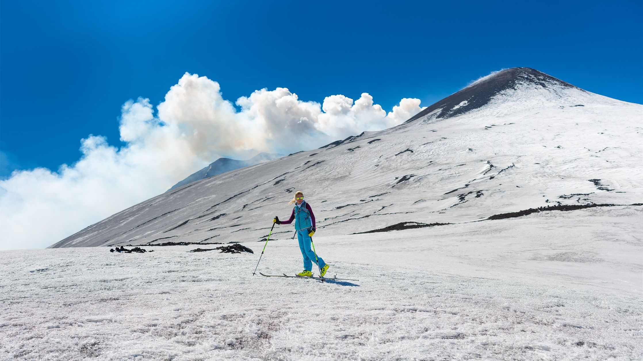 A woman skiing under the top of the crater of Mount Etna. 
