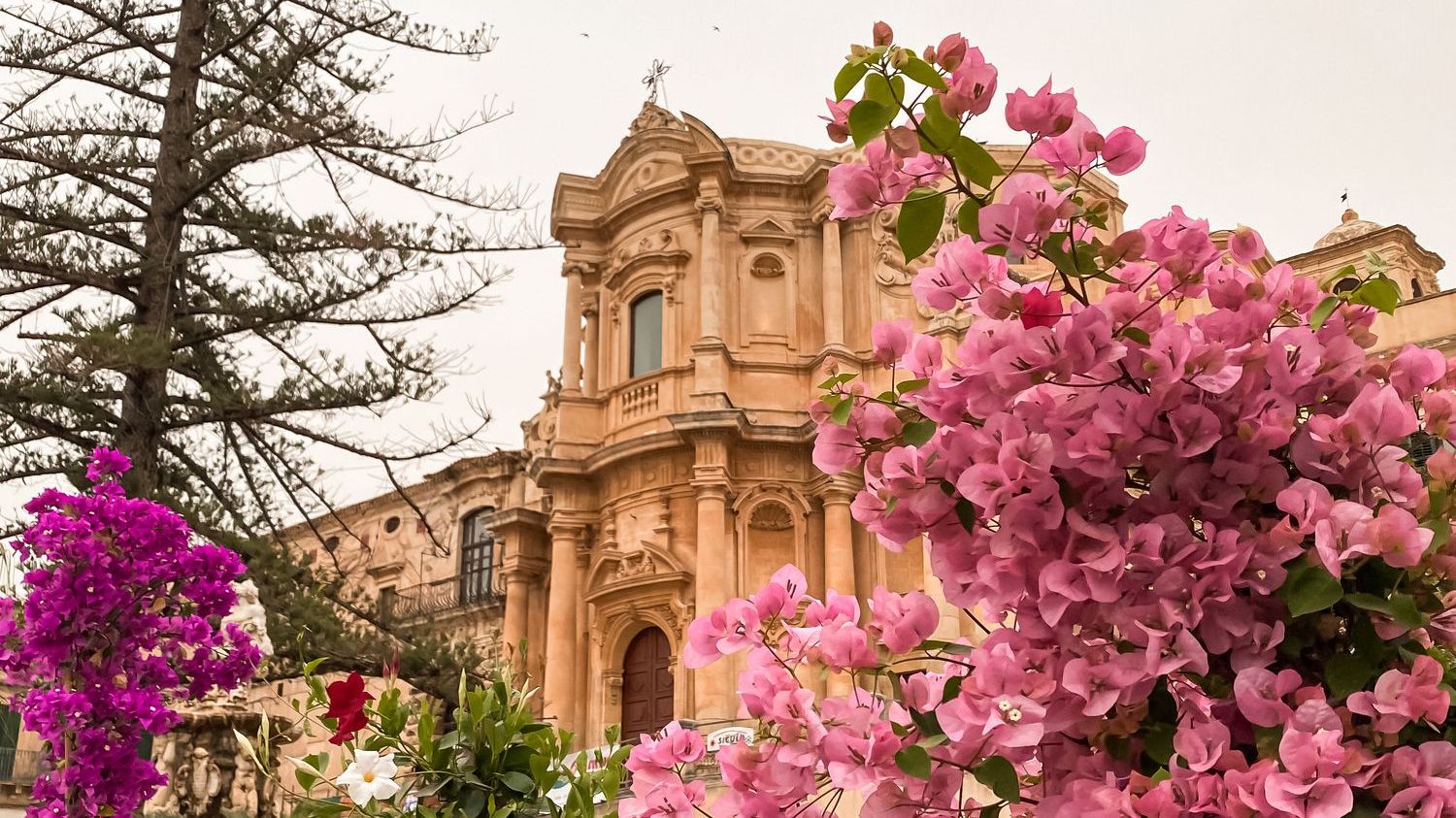 A Baroque church with pink flowers in the foreground. 