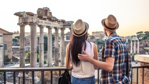 A young couple with their backs turned to the camera are admiring the Roman Forum in Rome.