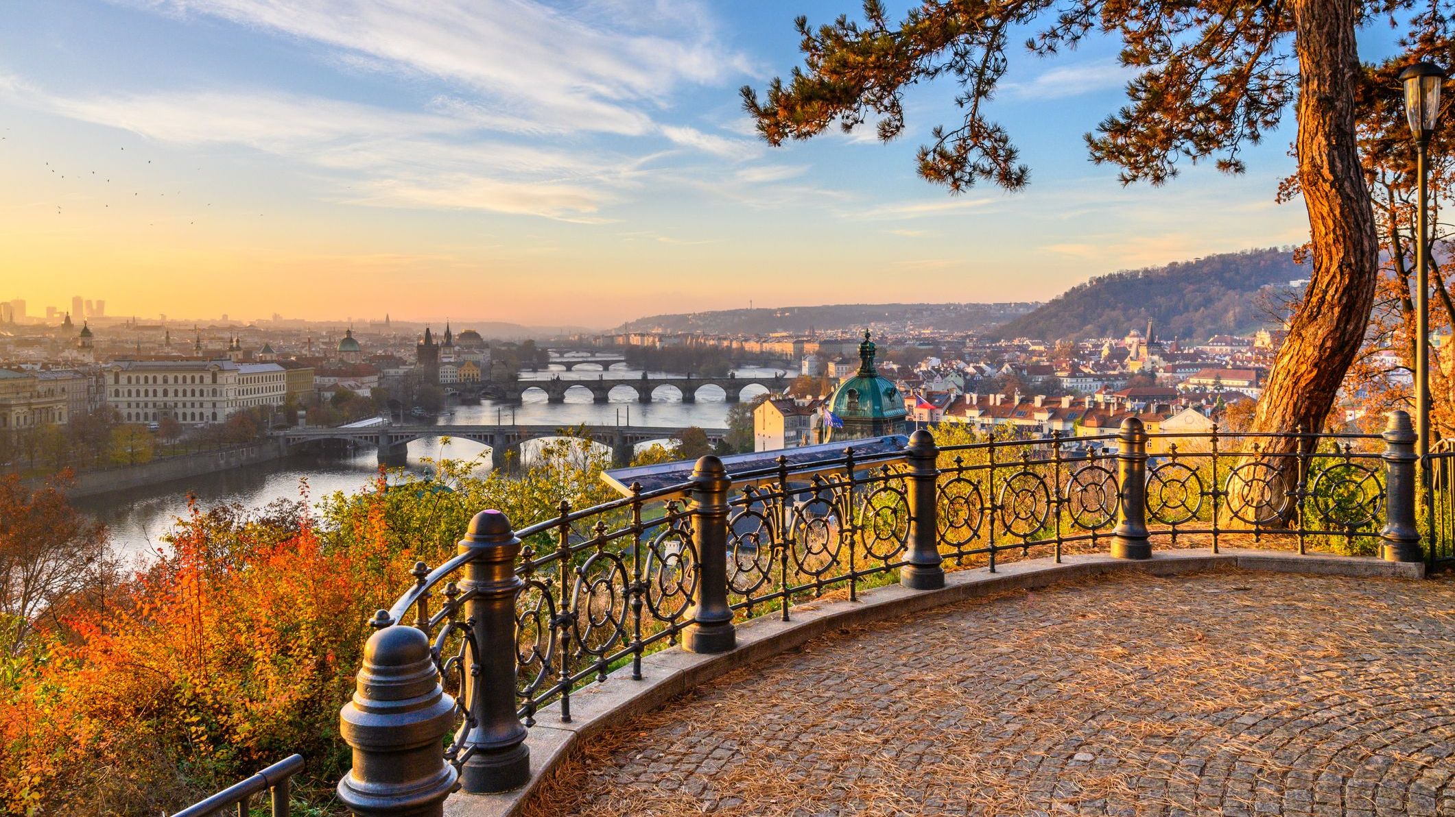 A panoramic view of Prague's bridges over the Vltava River as seen from Letna Park on a sunny autumn day.