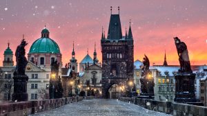 Sunrise over the Charles Bridge in Prague. The sky is pink and it's snowing.