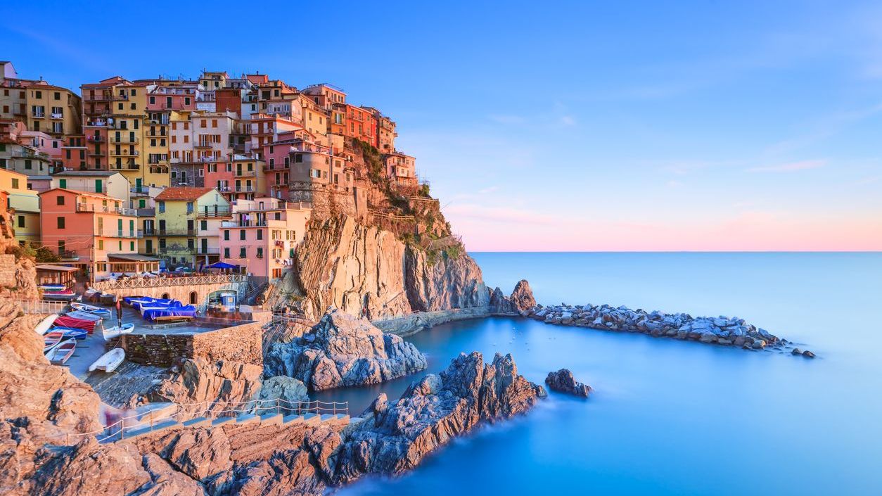 The pastel-colored buildings of Manarola village perched atop a hill overlooking the sea at sunset. 