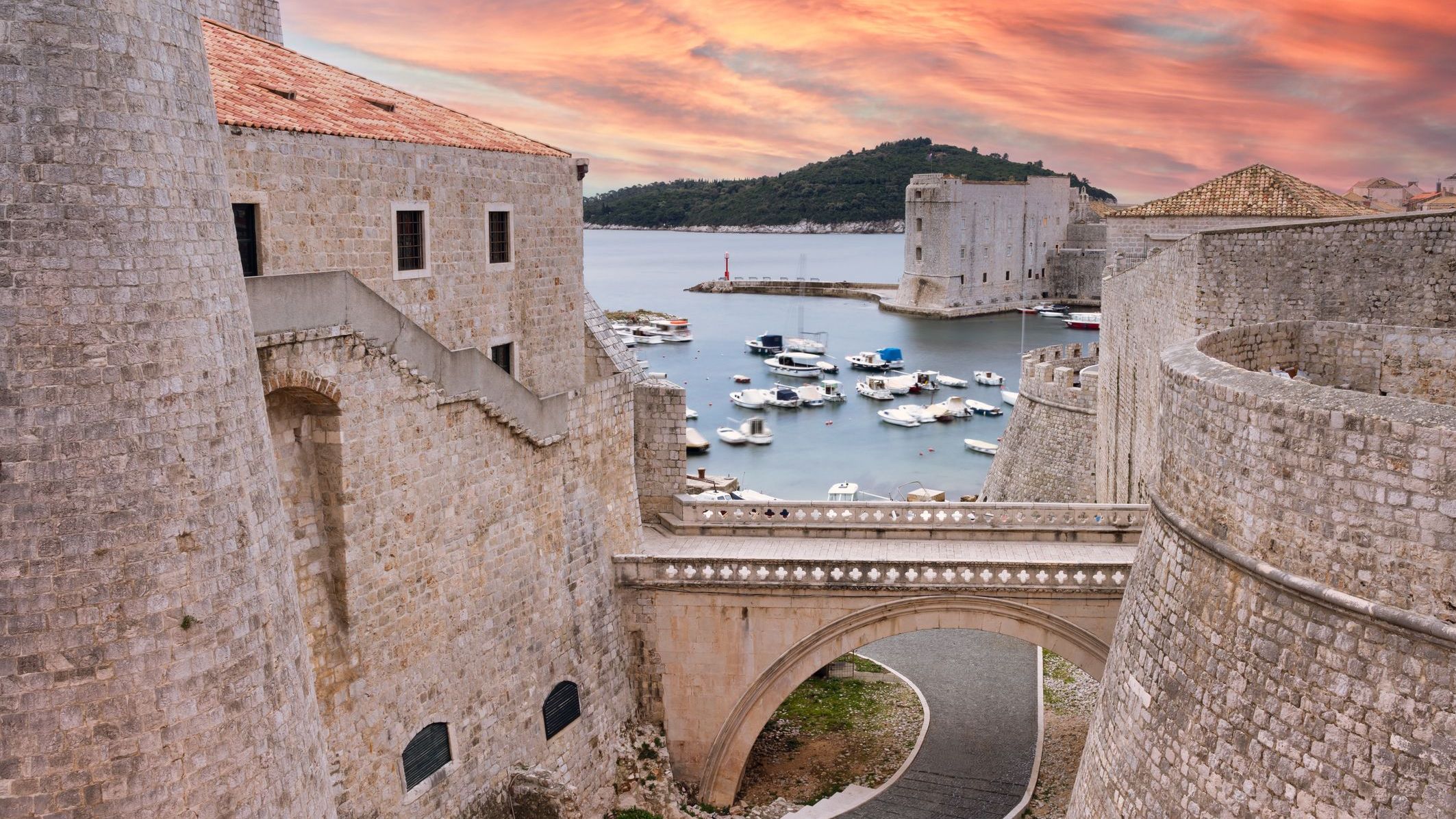 Dubrovnik's old city walls under a pink sunset sky. 