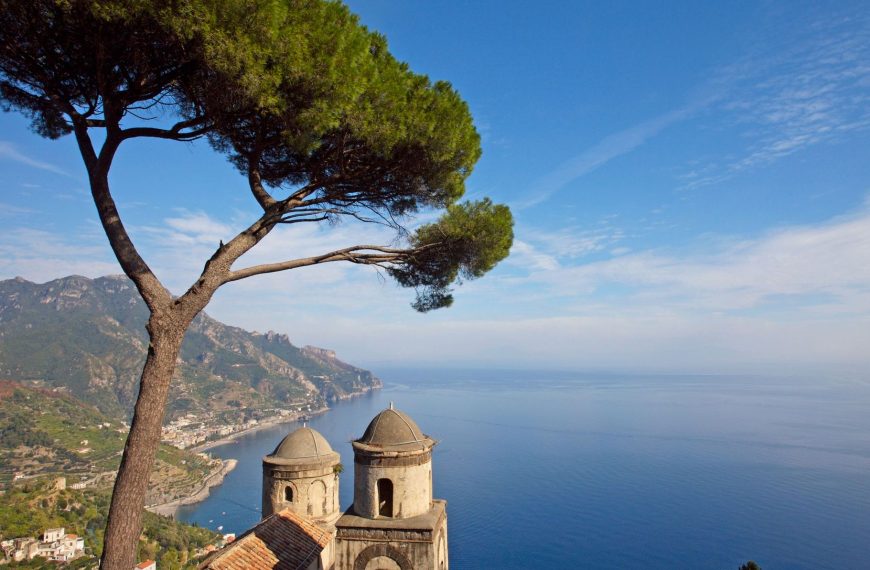 A typical Italian pine tree framing a magnificent view of the Mediterranean coast line from the beautiful gardens of Rufolo in Ravello with a stone church in the foreground.