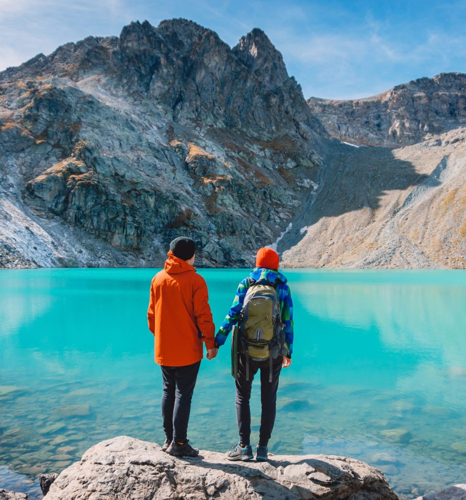 A couple holding hands by a turquoise alpine lake in Switzerland, surrounded by dramatic mountain peaks, enjoying a scenic outdoor adventure in the Swiss Alps.