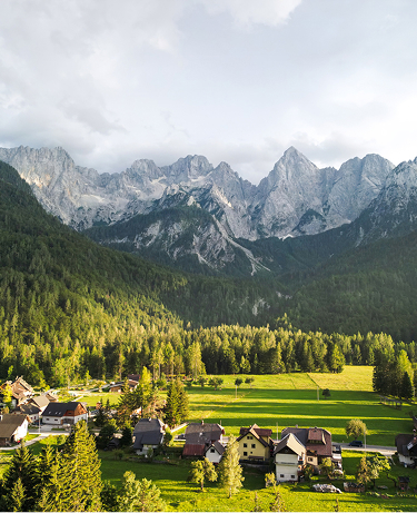 a valley with green forests and open fields, surrounded by mountain ranges. Sunlight breaks through the clouds, creating a soft contrast between light and shadow. Application: tourism, nature, ecology, travel, landscape design, advertising of eco-resorts or campsites.